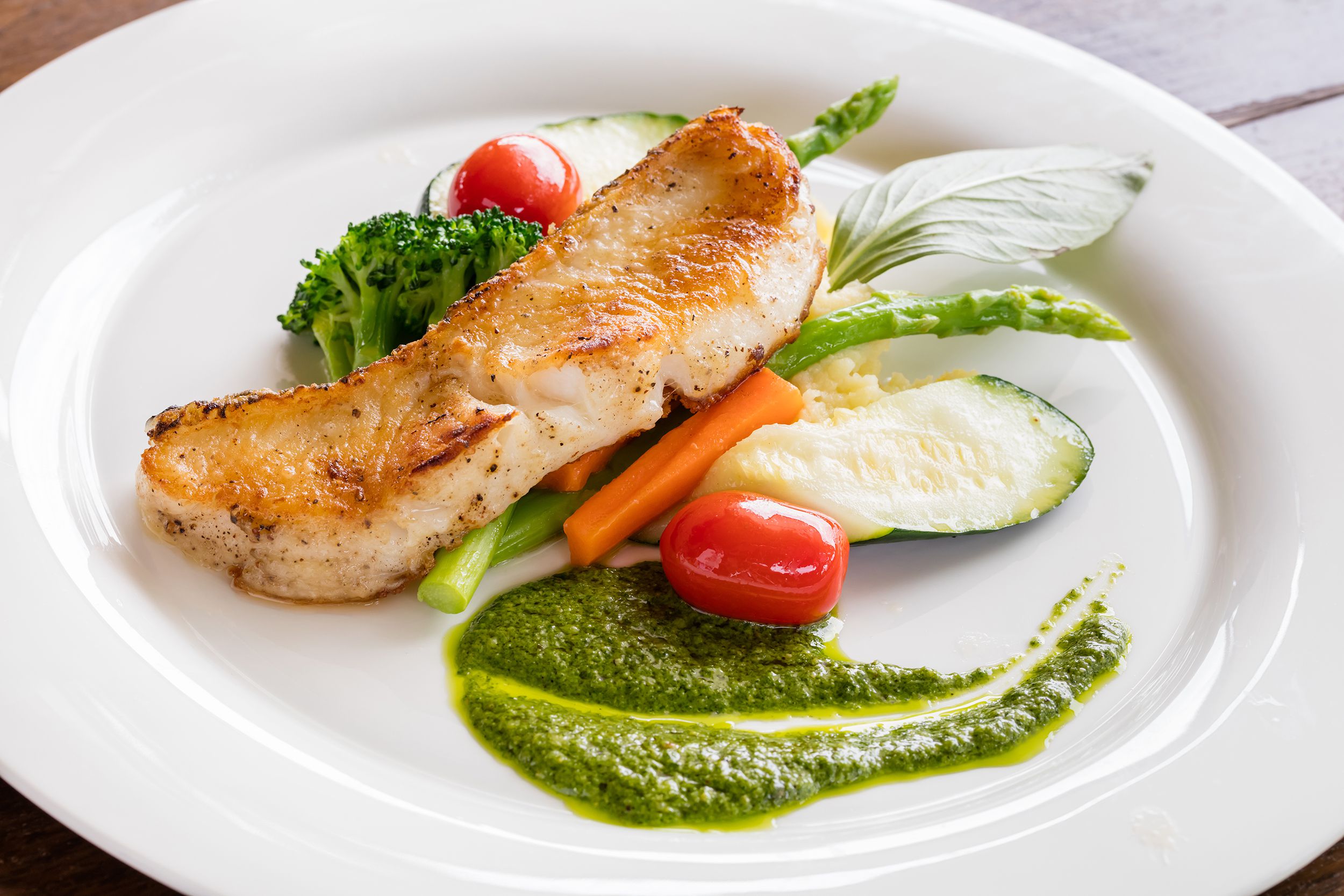 Whole grilled bluefish on a white porcelain plate, artistically arranged, with a table revealed in the corners of the image