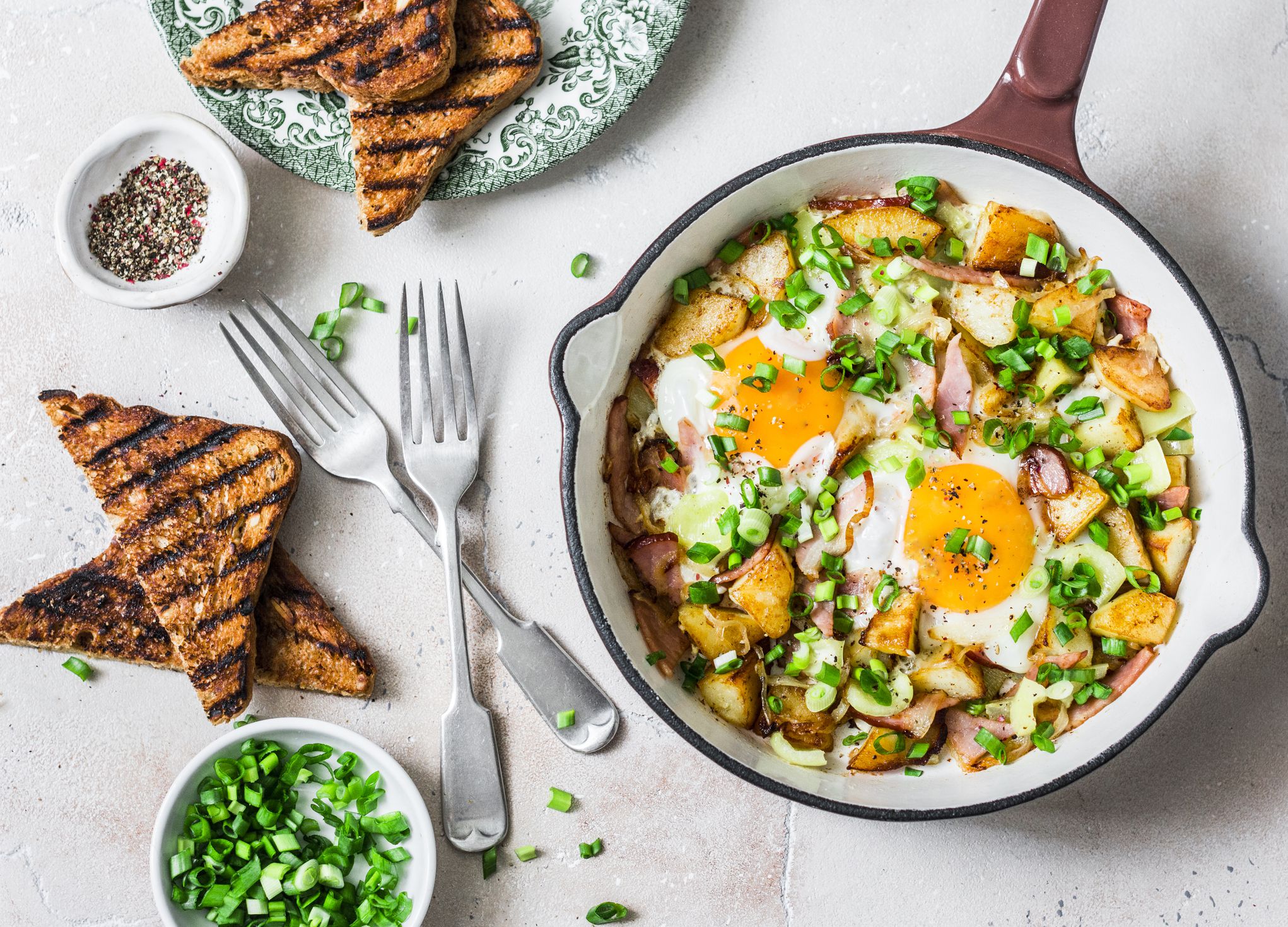 Potatoes, ham, eggs breakfast hash in a frying pan on a light background, top view. Delicious, nutritious breakfast, snack