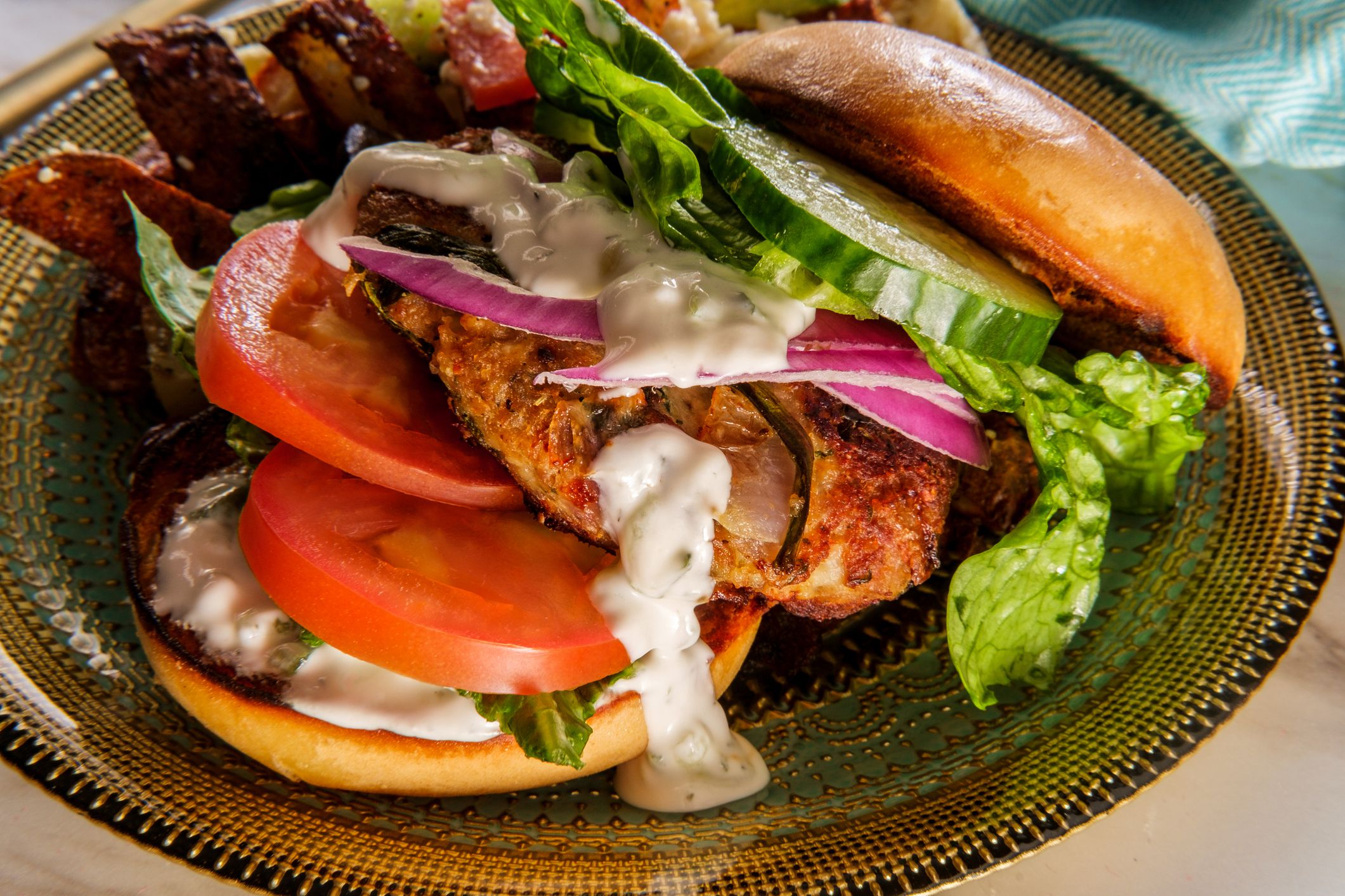 Greek stuffed turkey burger topped with cucumber slices and tzatziki yogurt sauce served with Mediterranean street cart fried potatoes with feta cheese olives herbs and spices
