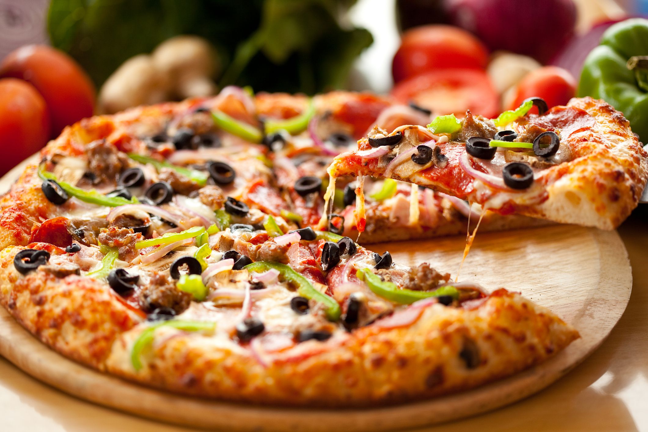A slice of freshly baked supreme pizza, lifted from the entire pie.