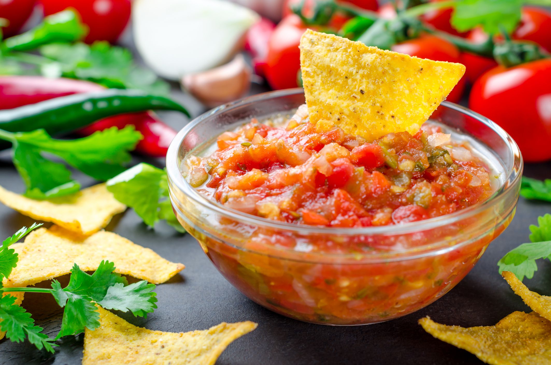 Traditional mexican homemade salsa sauce with ingredients, tomatoes, pepper, cilantro, chips on a dark black stone table. Close-up, horizontal image