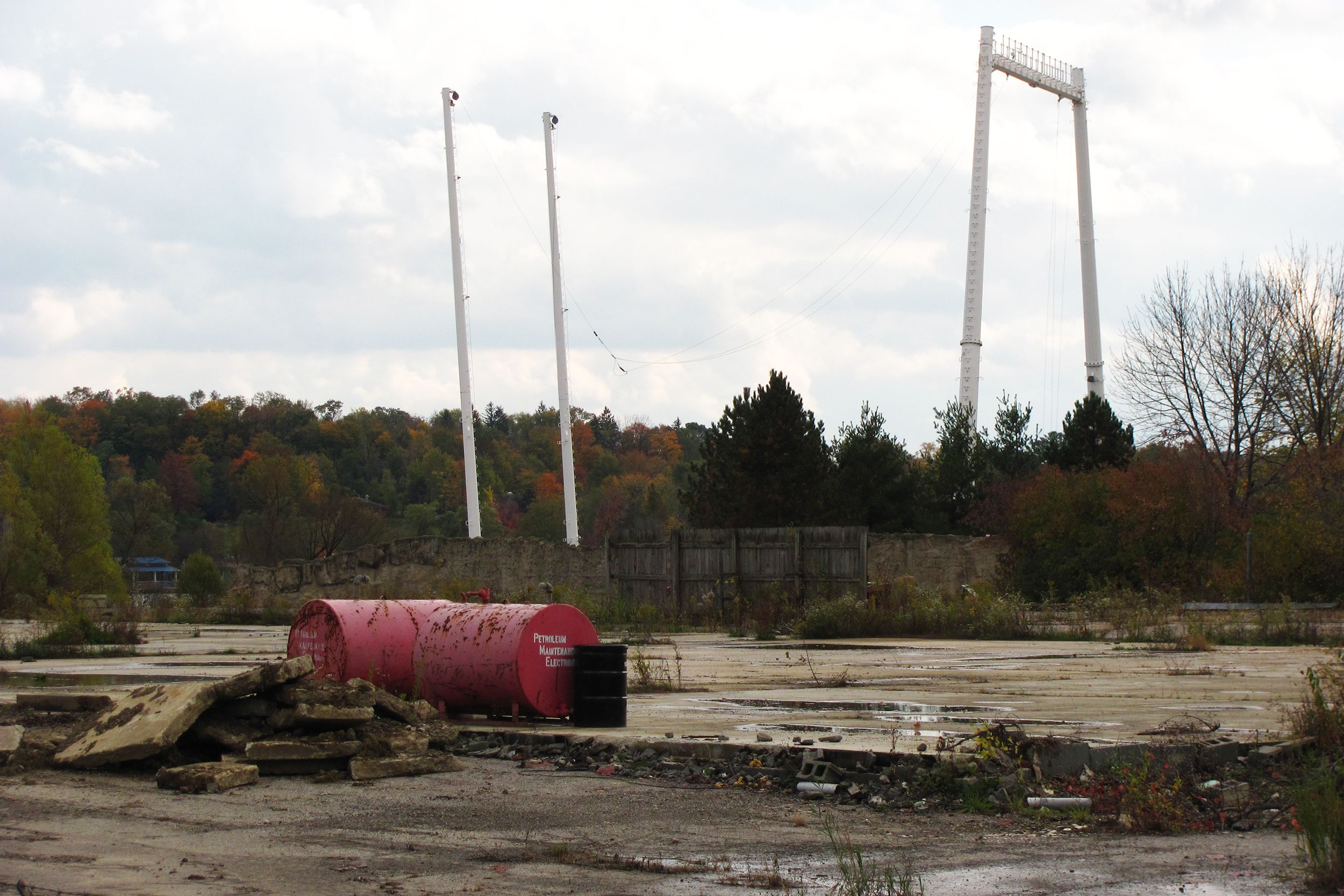 Abandoned Geauga Lake Park, Aurora, Ohio, two pairs of white beams of a once ride, red barrels and broken blocks in the foreground, trees in a forest, during early autumn, in the background, a blue sky with white clouds