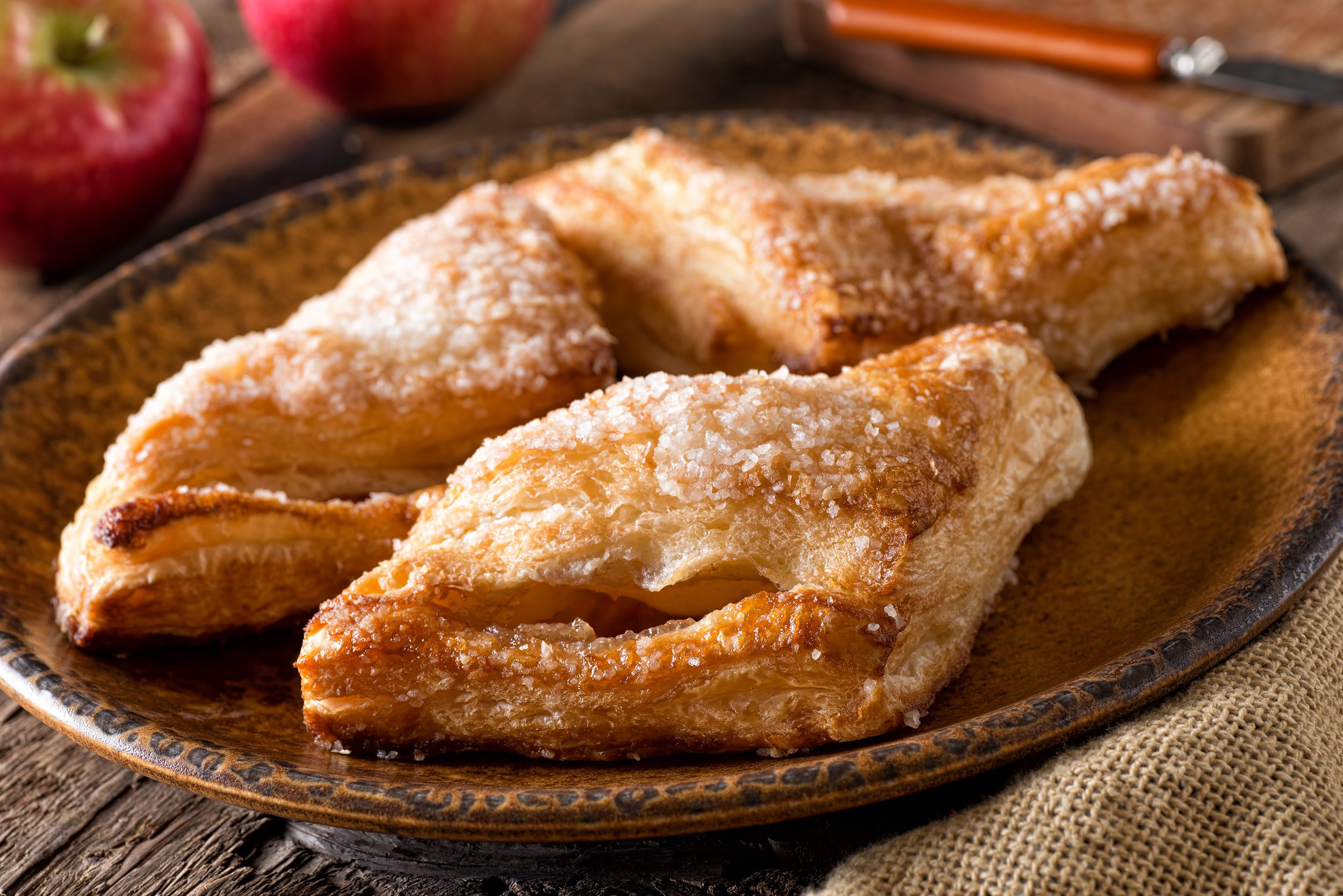 Paula Deen air fried apple pies on a brown earthenware plate on wooden table with rustic background