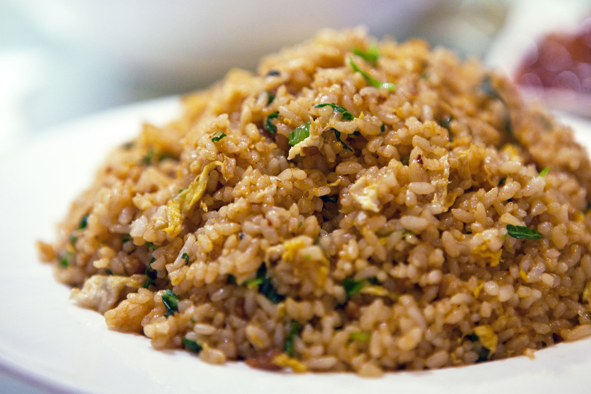 Closeup of air fried rice with sesame-sriracha sauce on a white plate with blurred background
