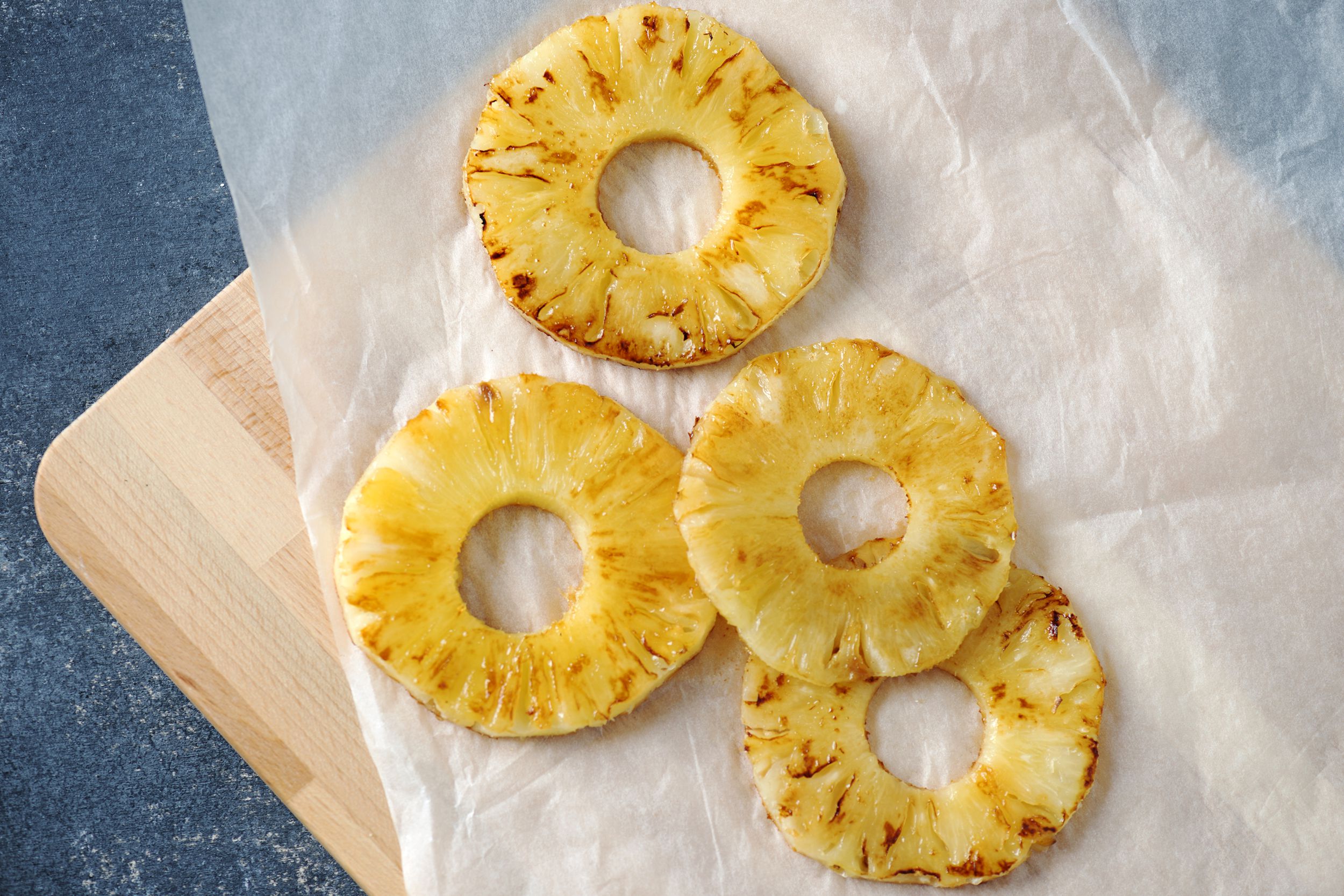Four slices of air fryer Brazilian grilled pineapple on a cooking sheet on a cutting board on a blue table