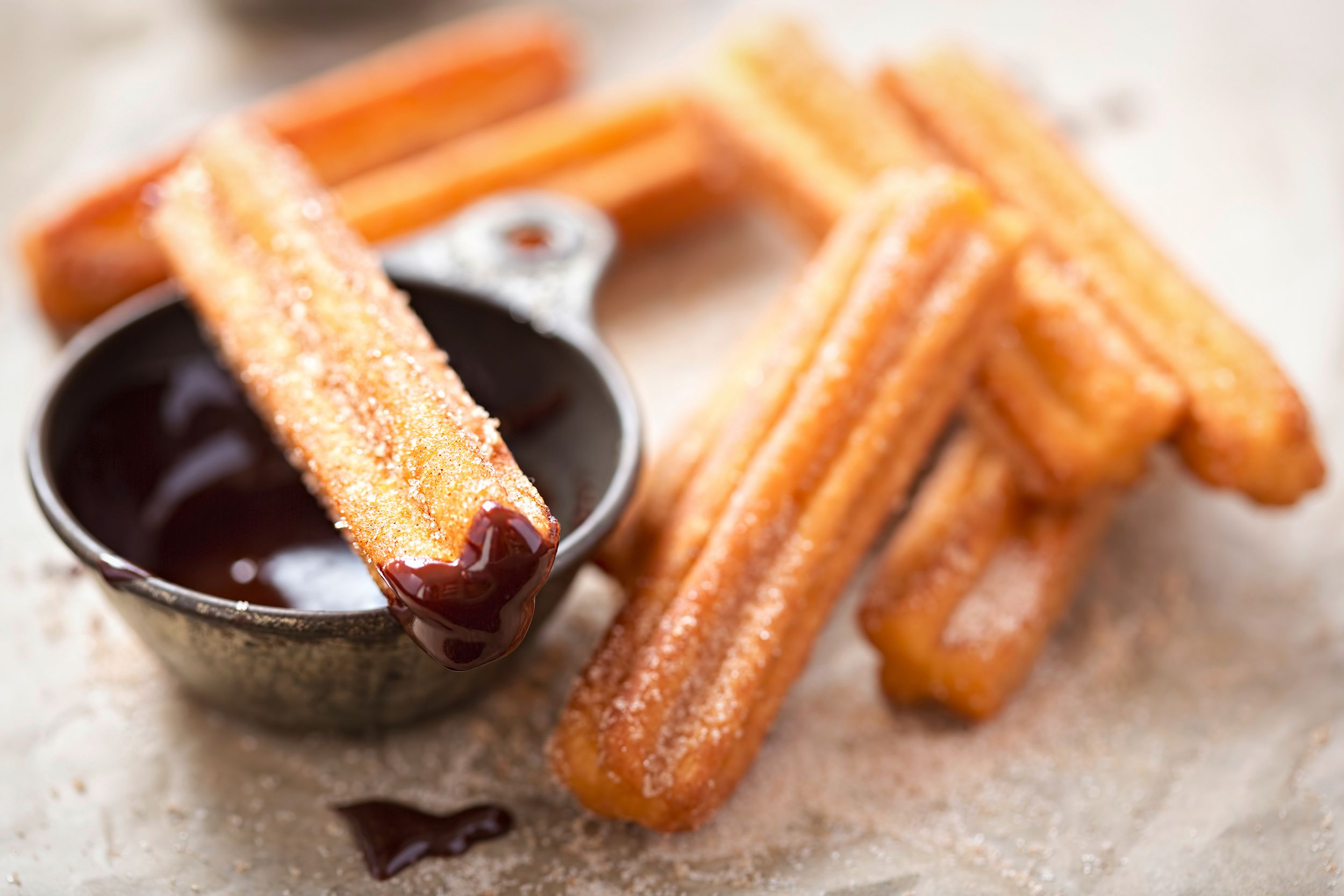 Closeup of air fryer churros with chocolate sauce, one churro is dipped in chocolate sauce with blurred background