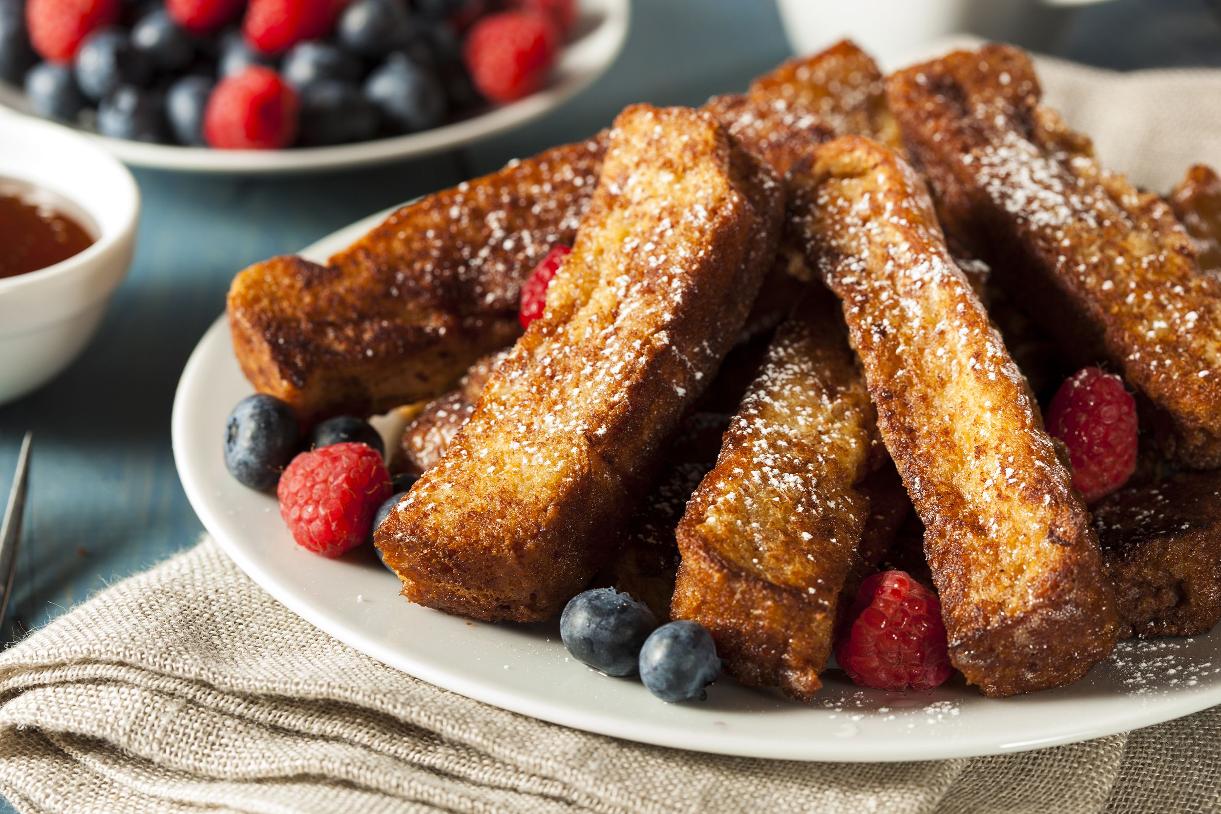 Air fryer french toast sticks with blueberries and raspberries on a white plate with maple syrup and berries in the background