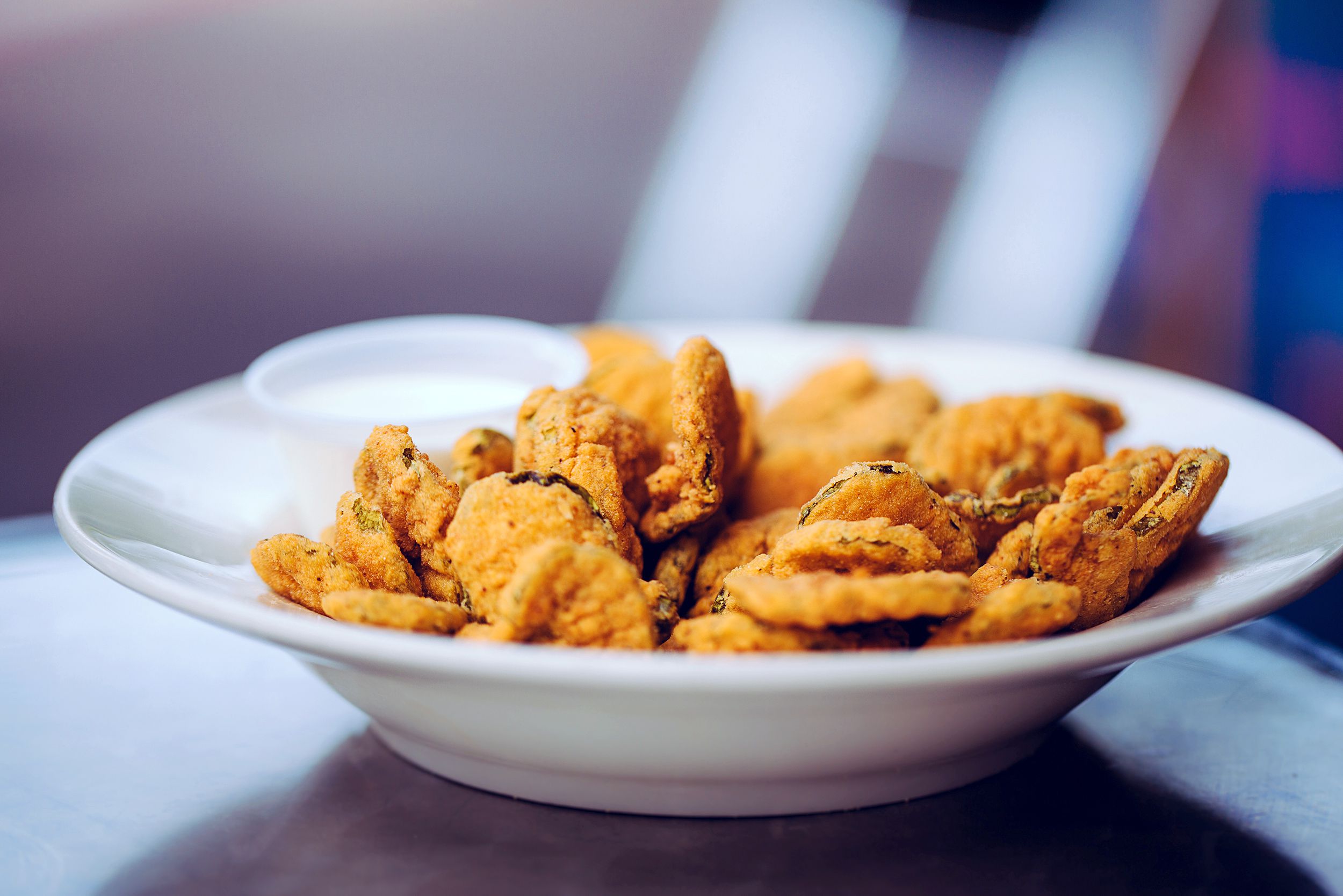 Air fryer pickles with white sauce in a white bowl with blurred background