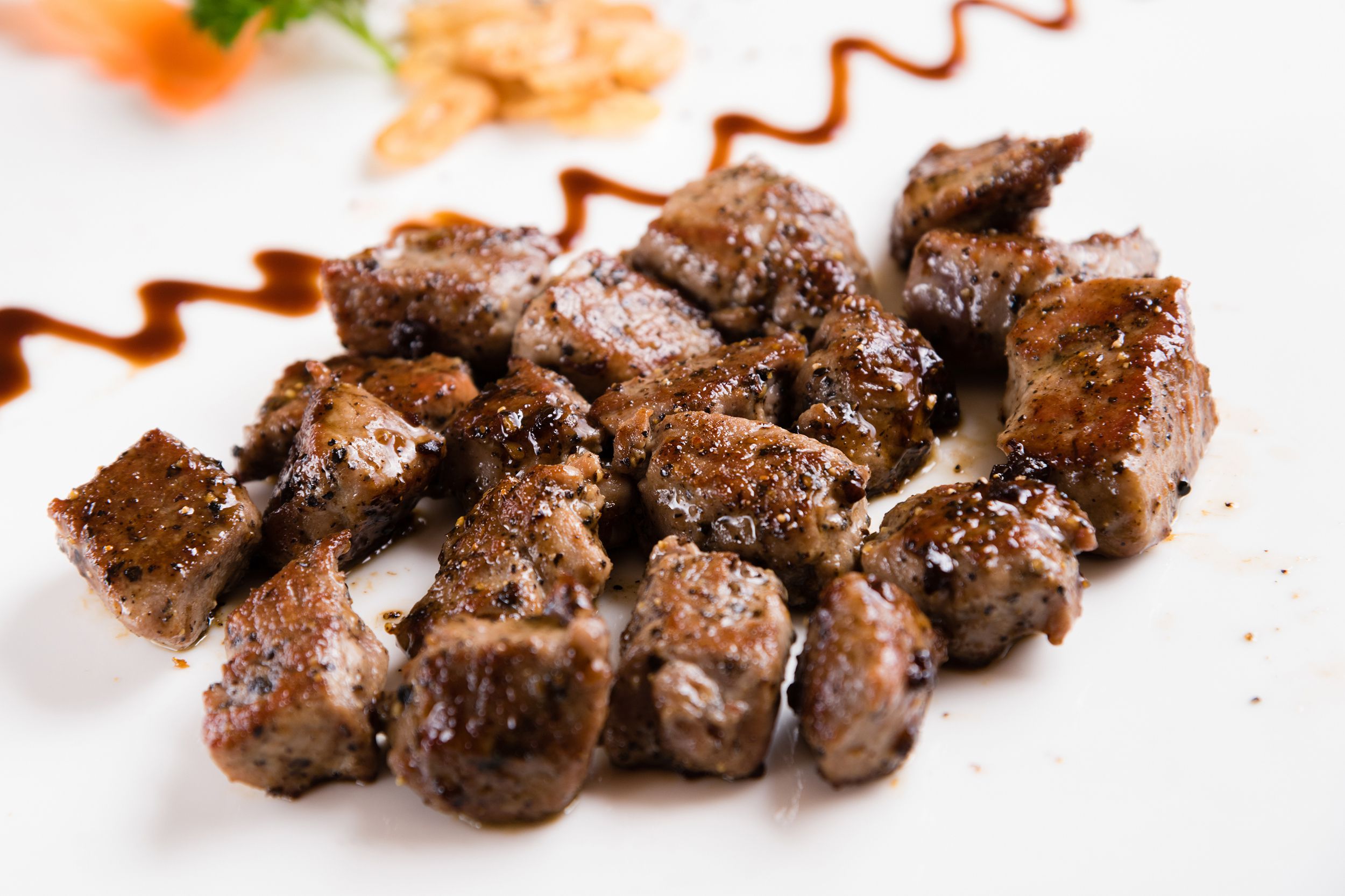 Air fryer steak bites on a white plate with blurred decorative garnishing in the background