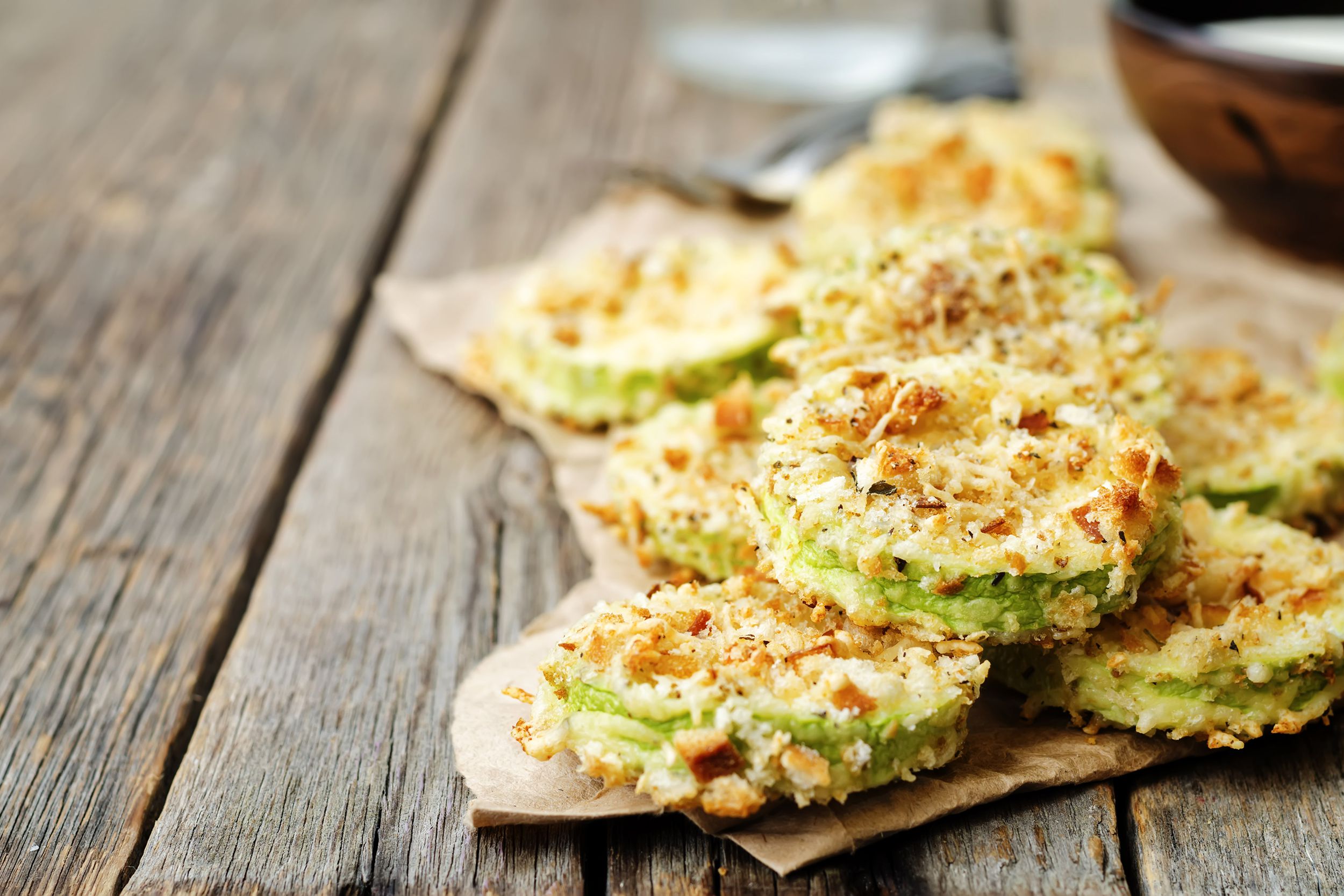 Air fryer zucchini parmesan crisps on brown paper on wooden table with blurred background