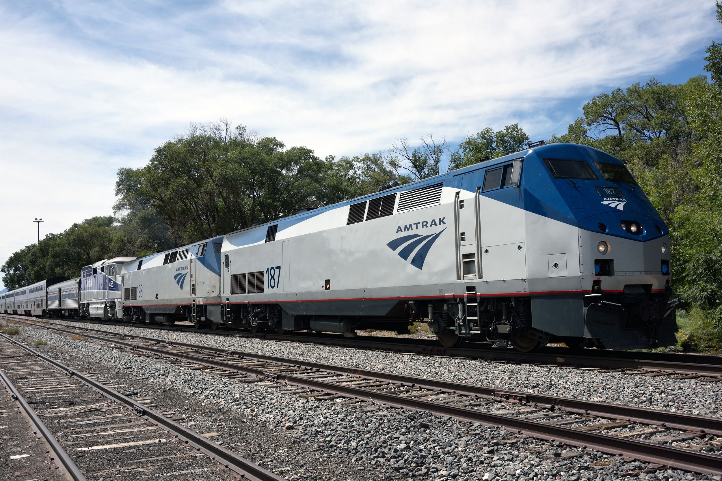 The eastbound Amtrak Southwest Chief passenger train stationed at Lamy, New Mexico with trees and white clouds in a sunny blue sky in the background