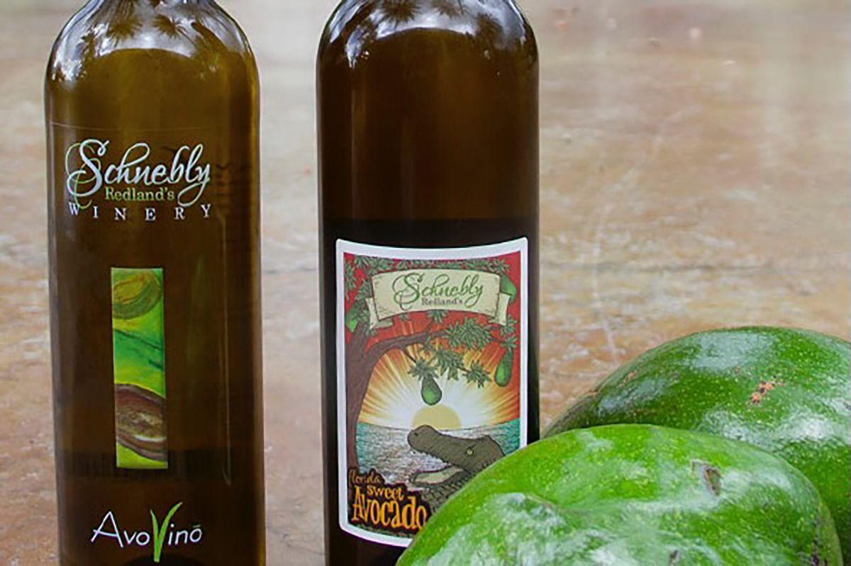 Two fresh avocados in front of two bottles of avocado wine.