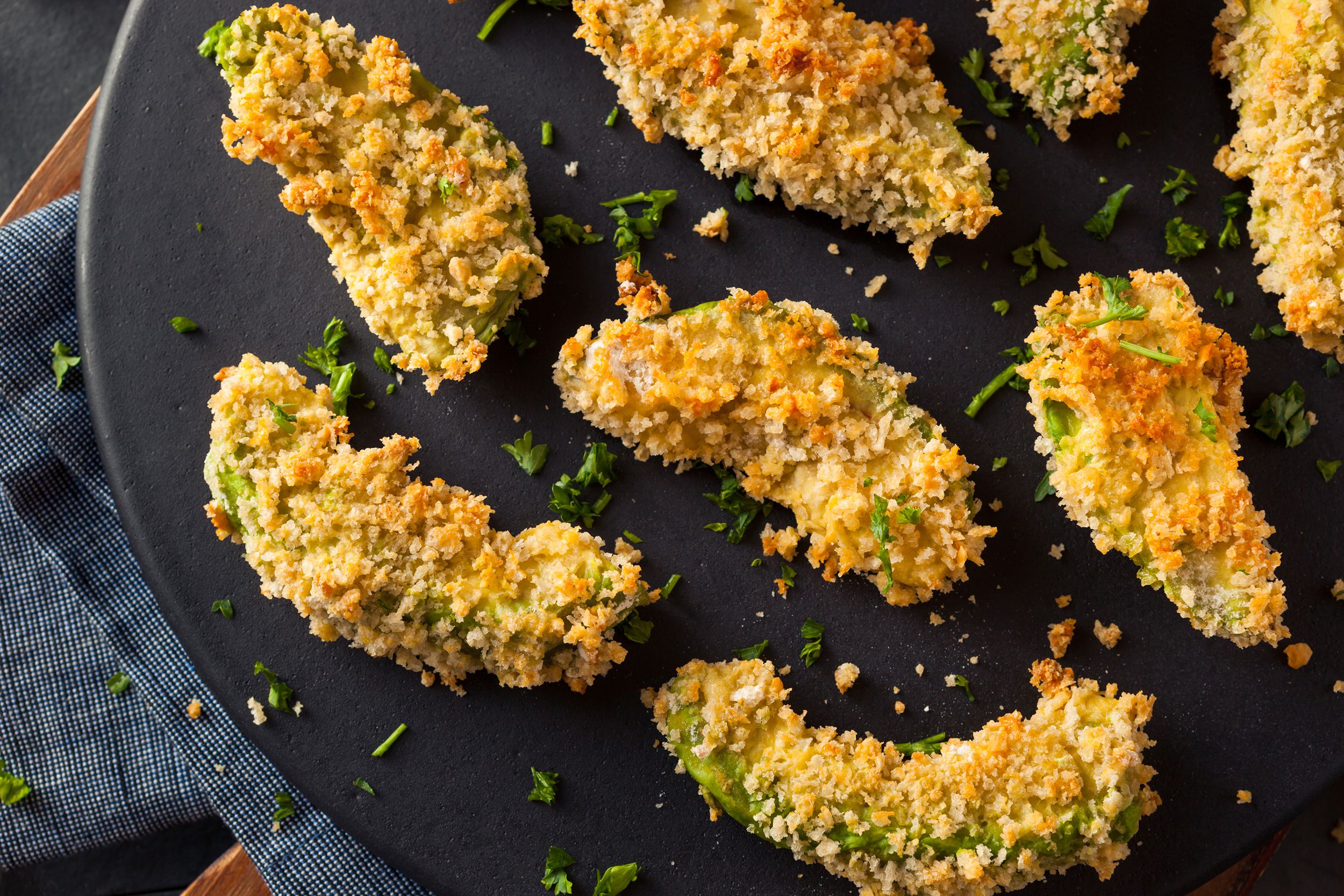 Crispy air fried avocado fries on black plate with garnish