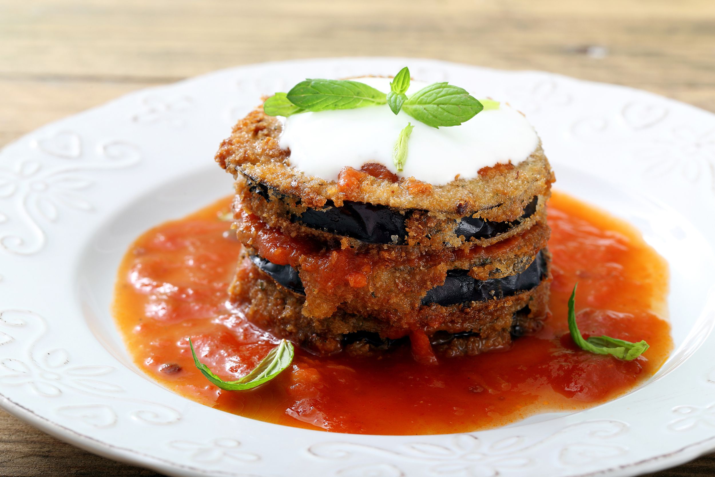 Crispy air fryer eggplant parmesan decorated with herbs and a delicate marinara sauce on a white plate with wooden table background