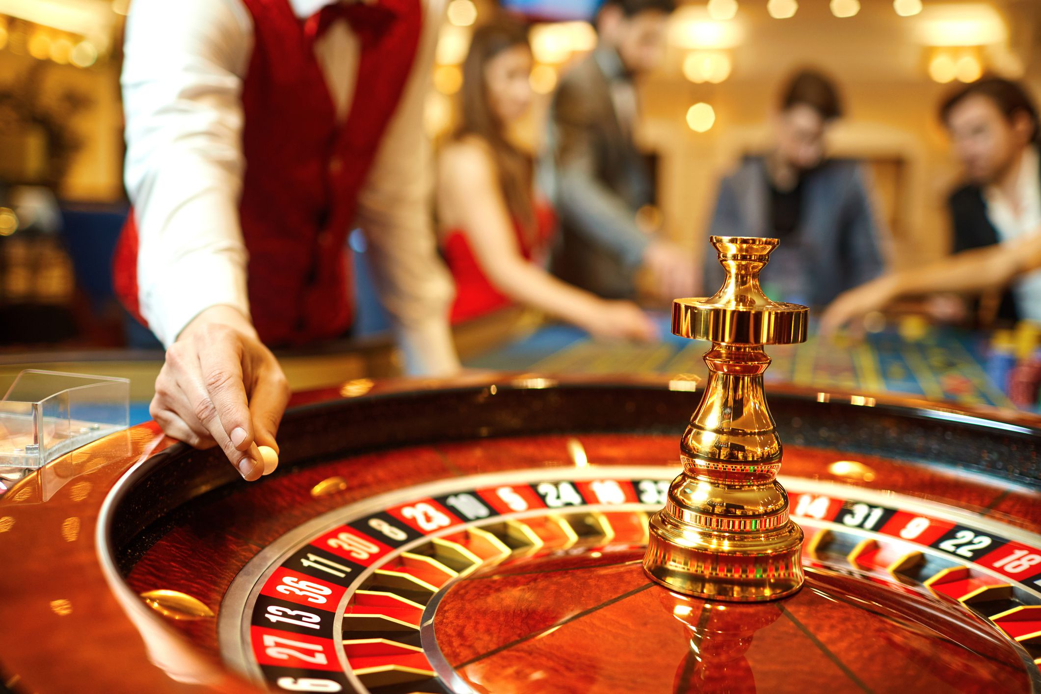 A croupier holds a roulette ball in a casino in his hand, selective focus, roulette wheel in the foreground, a group of players at the table blurred in the background