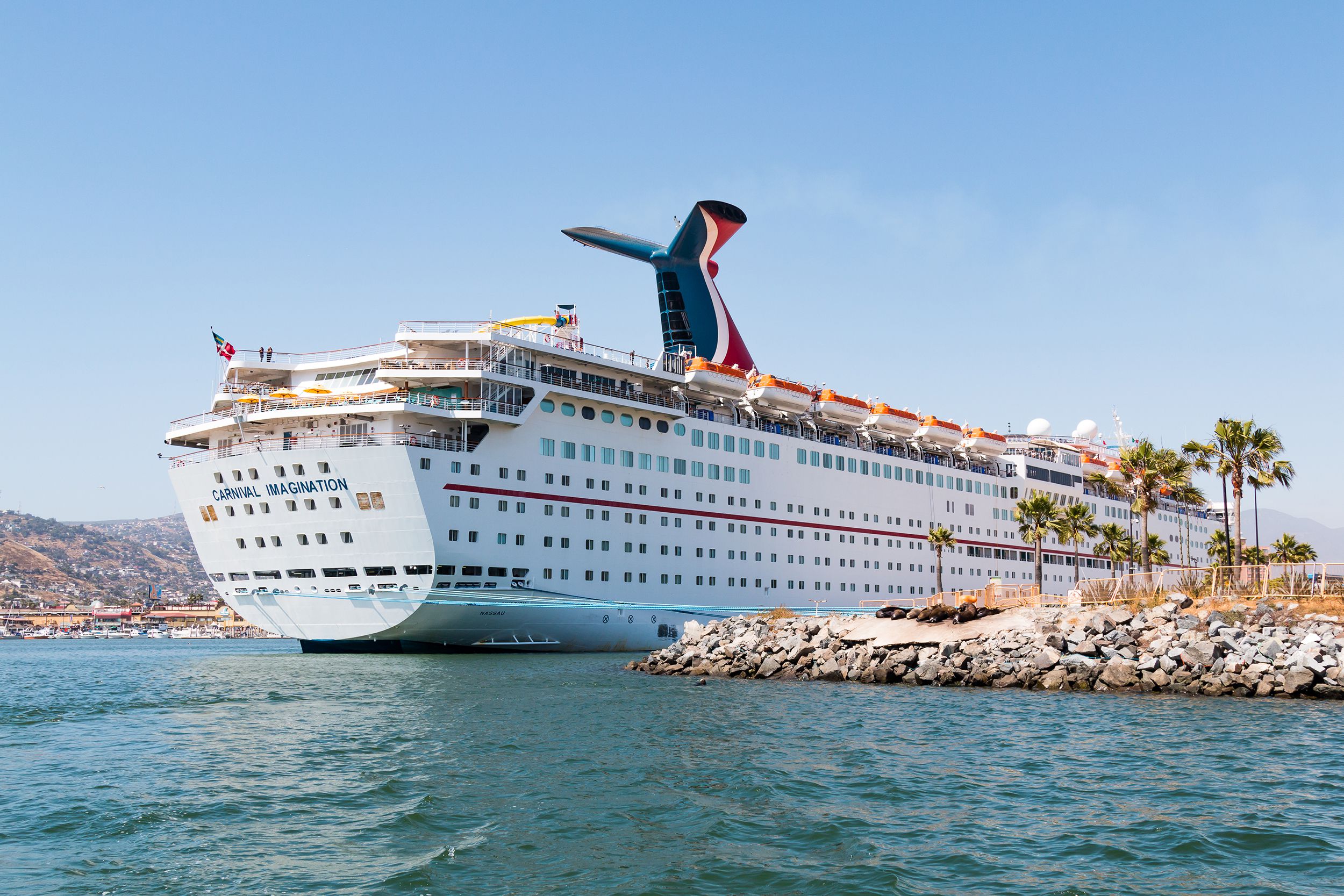 Cruise ship Carnival Imagination docked in the Port of Ensenada, Mexico, ocean in the foreground and blue sky in the background, on a sunny day