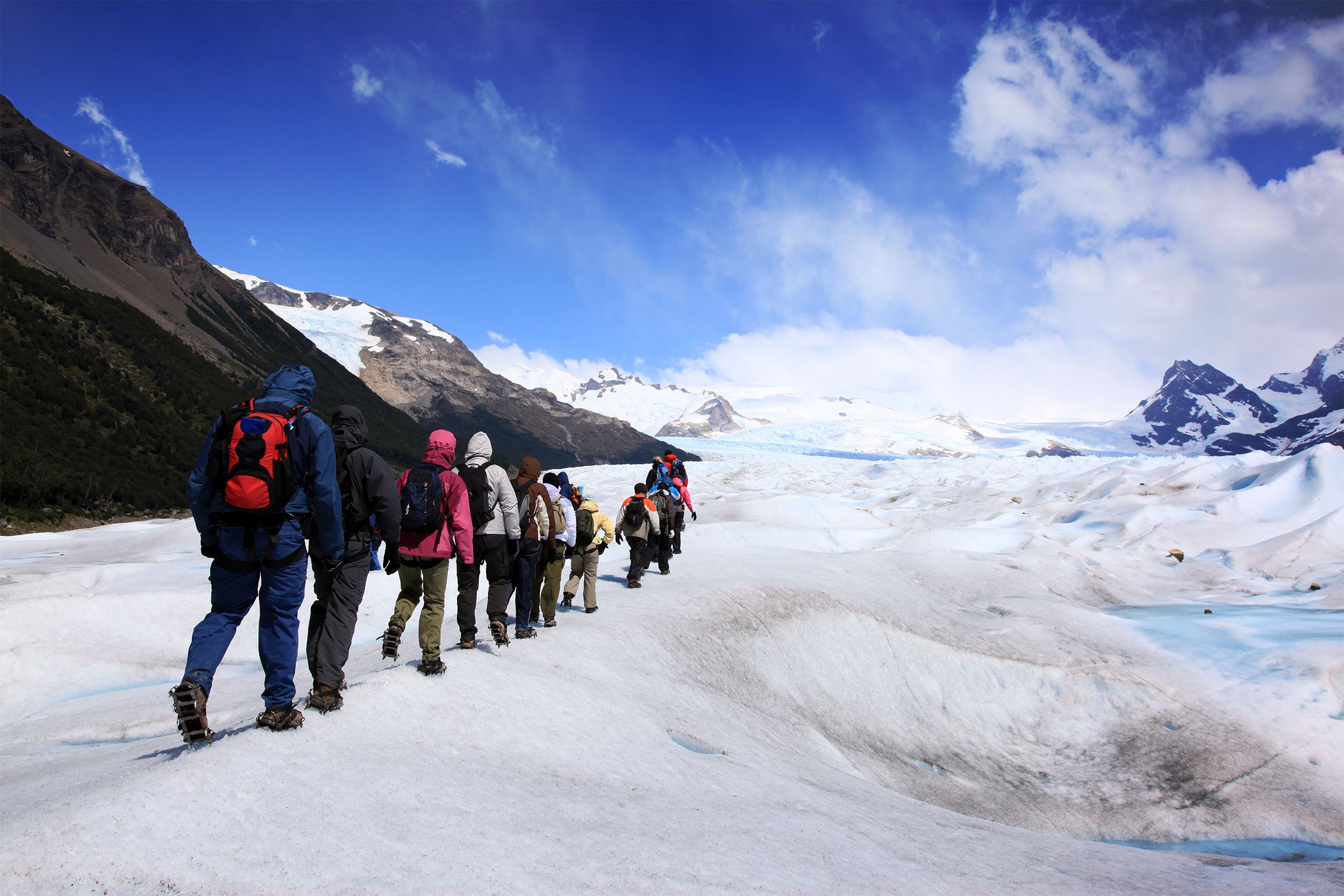 A line of people hiking on Perito Moreno Glacier, Argentina, all wearing snow gear, bright sunny day against the white snow