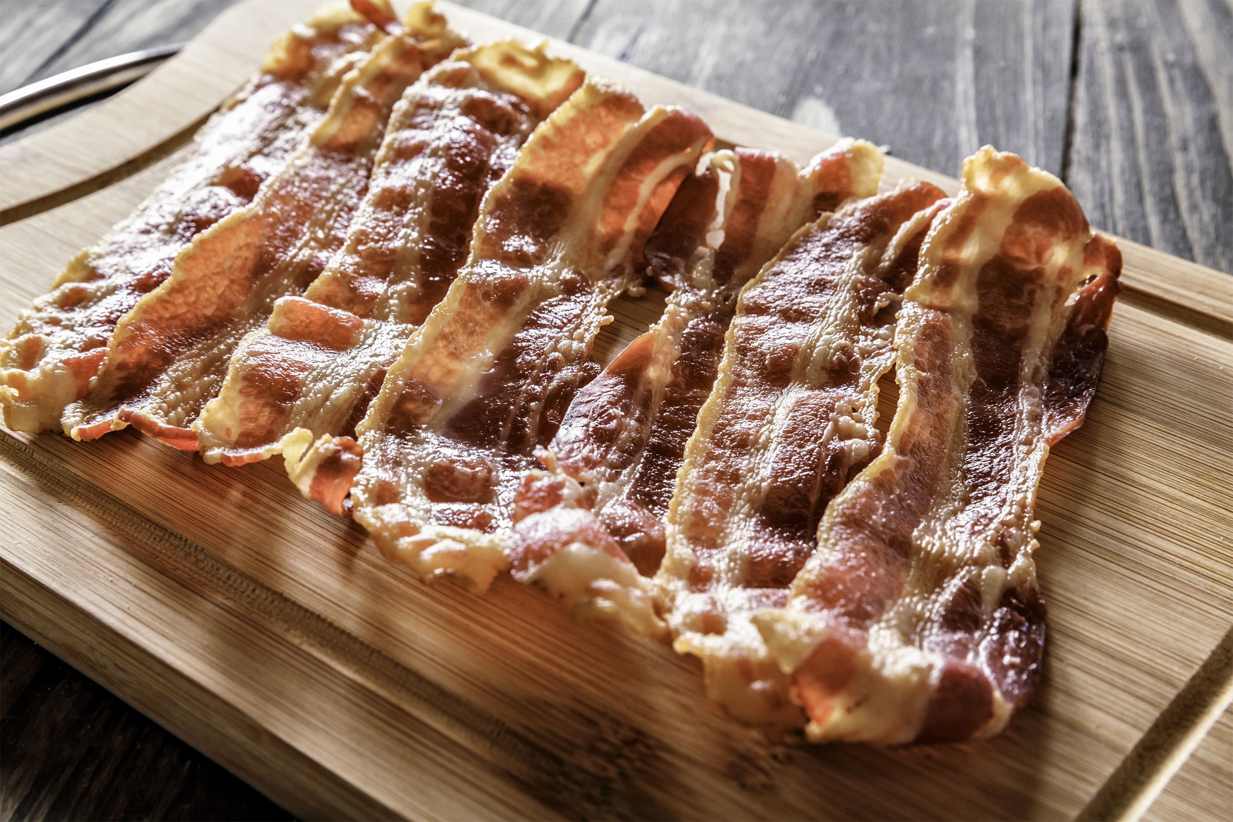 Several pieces of air fryer bacon on a wooden cutting board with wooden table background