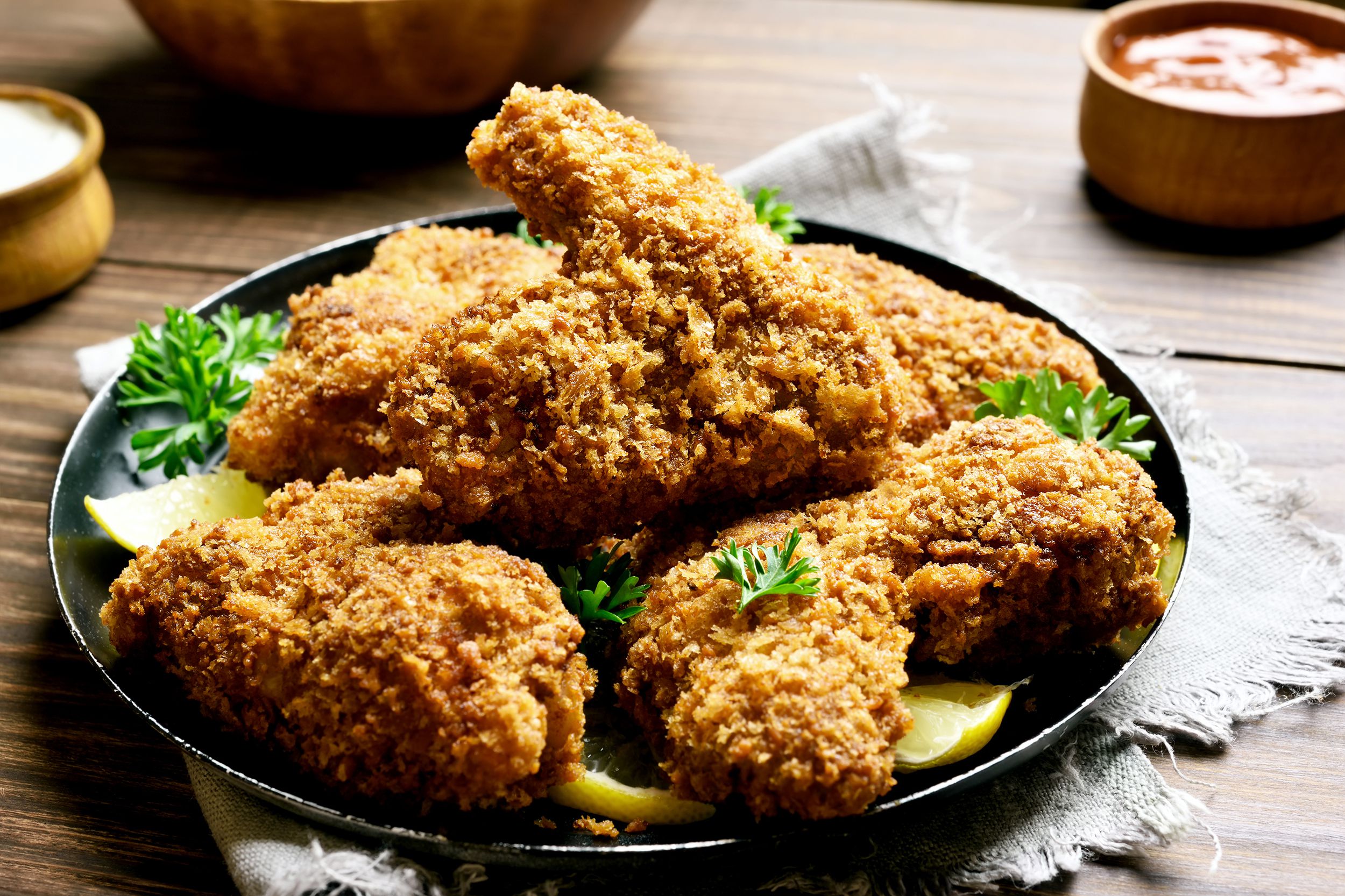 Bowl of un-fried chicken with lemons and garnish on table with condiments in the background