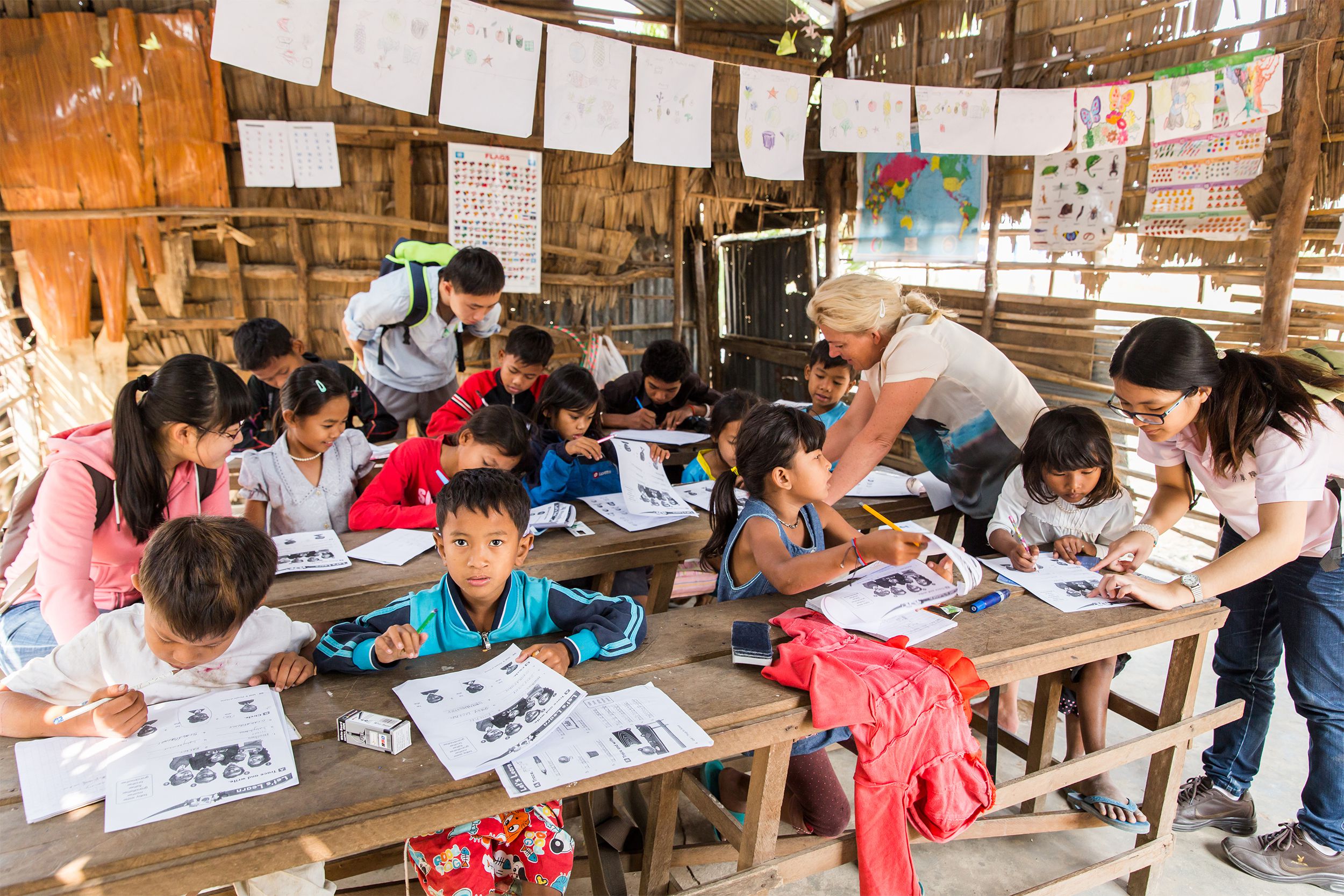 Four adult volunteers assisting local elementary students having an english lesson at the school, New Bridge for Cambodia, Siem Reap, Cambodia, students are sitting at three rows of desks