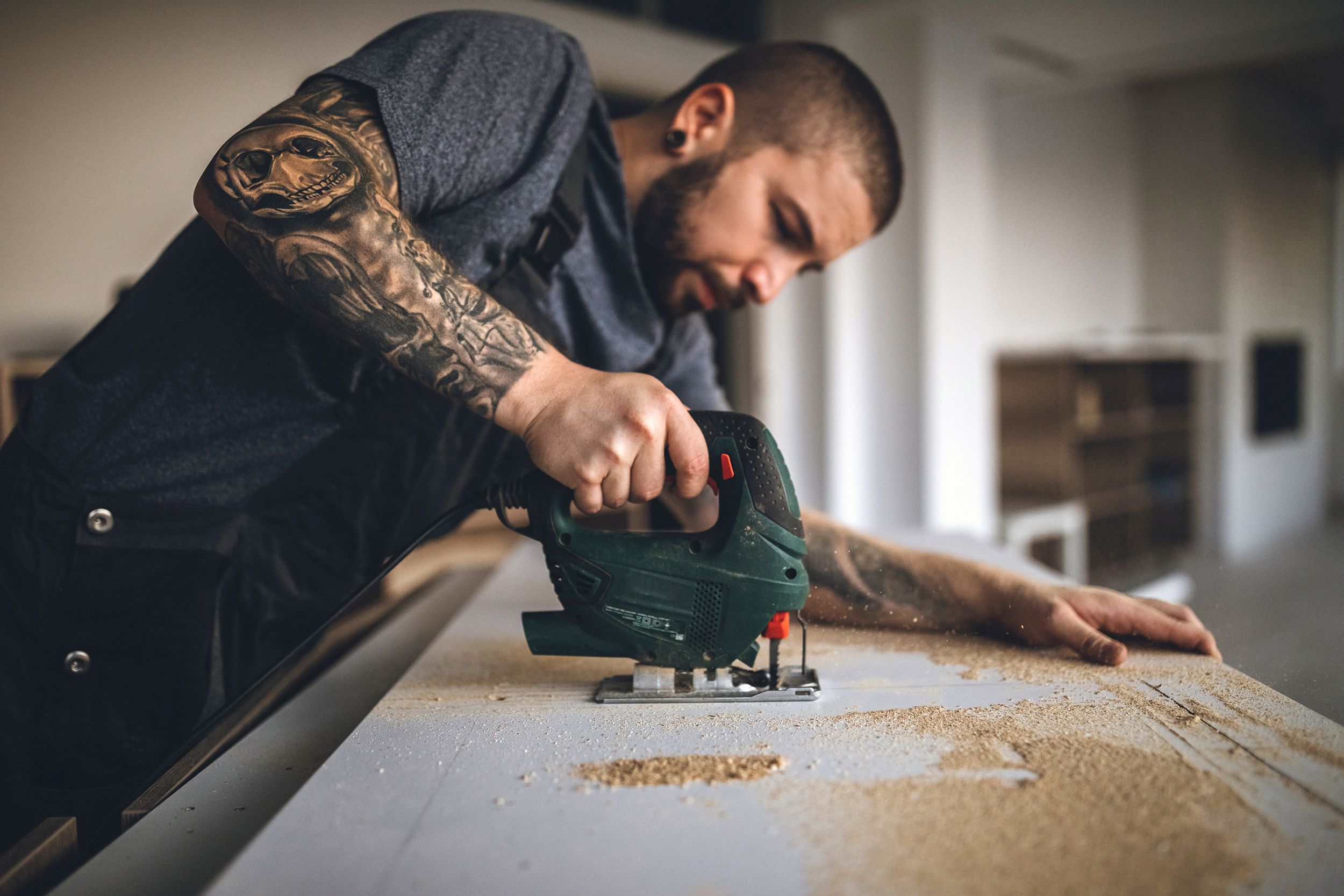 tattooed handy man drilling plank and fixing new wooden table