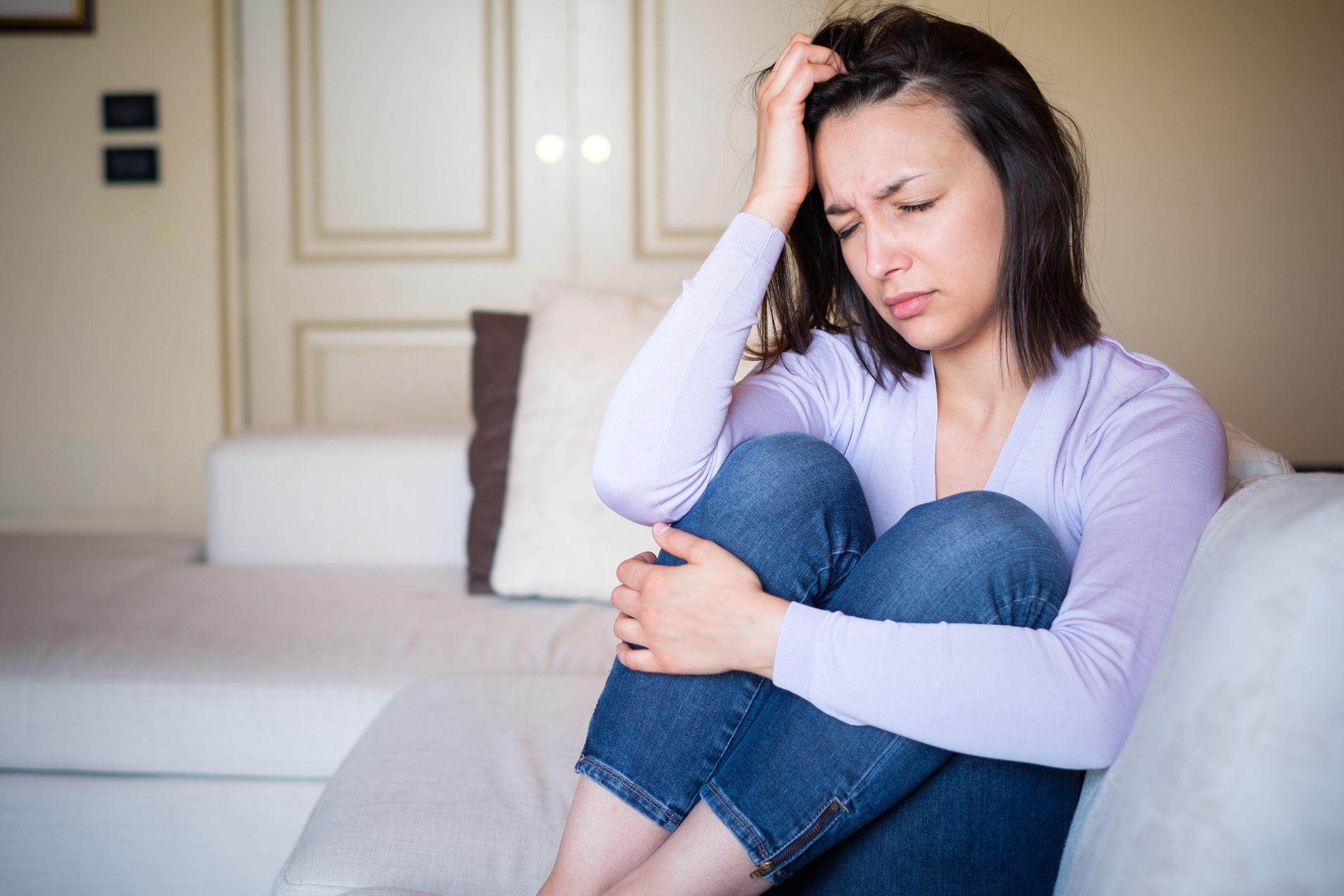 young woman looking pained with hand to her head, sitting on couch