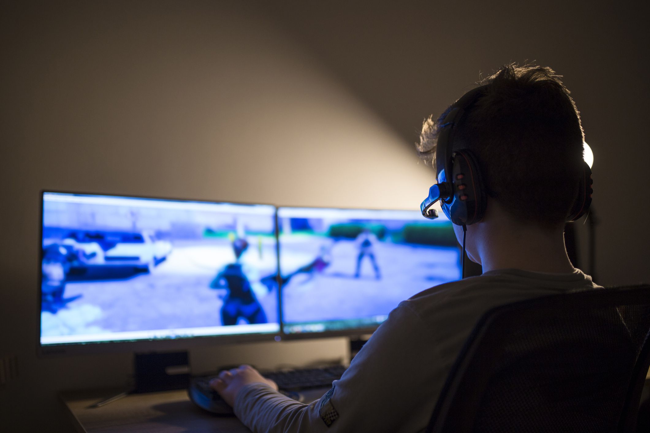 boy playing computer games with headset, two desktop monitors