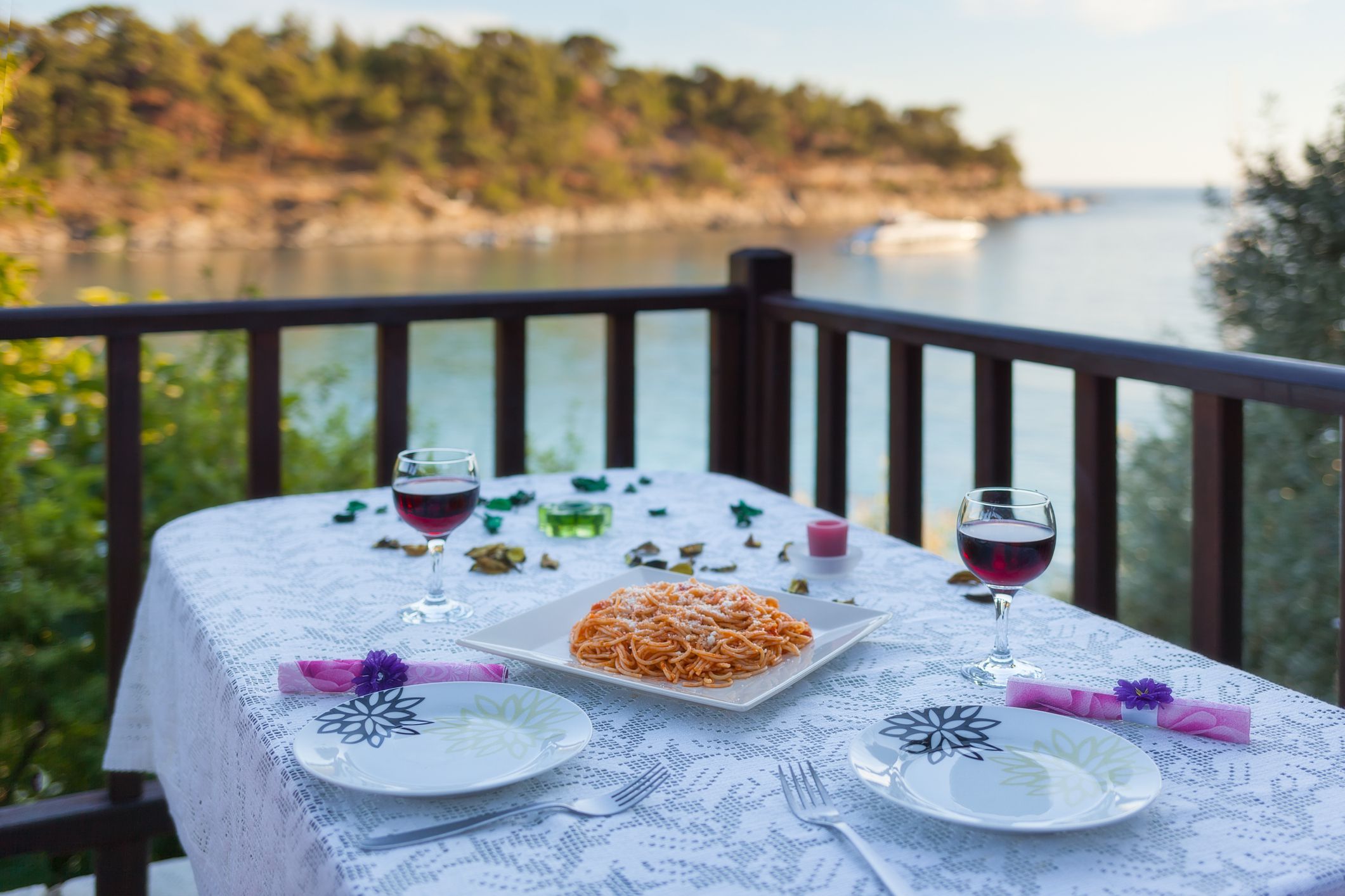 Sea wiew dinner setting at romantic sunset atmosphere with dining table setup for couple with spaghetti and wine glasses. Shallow depth of field.