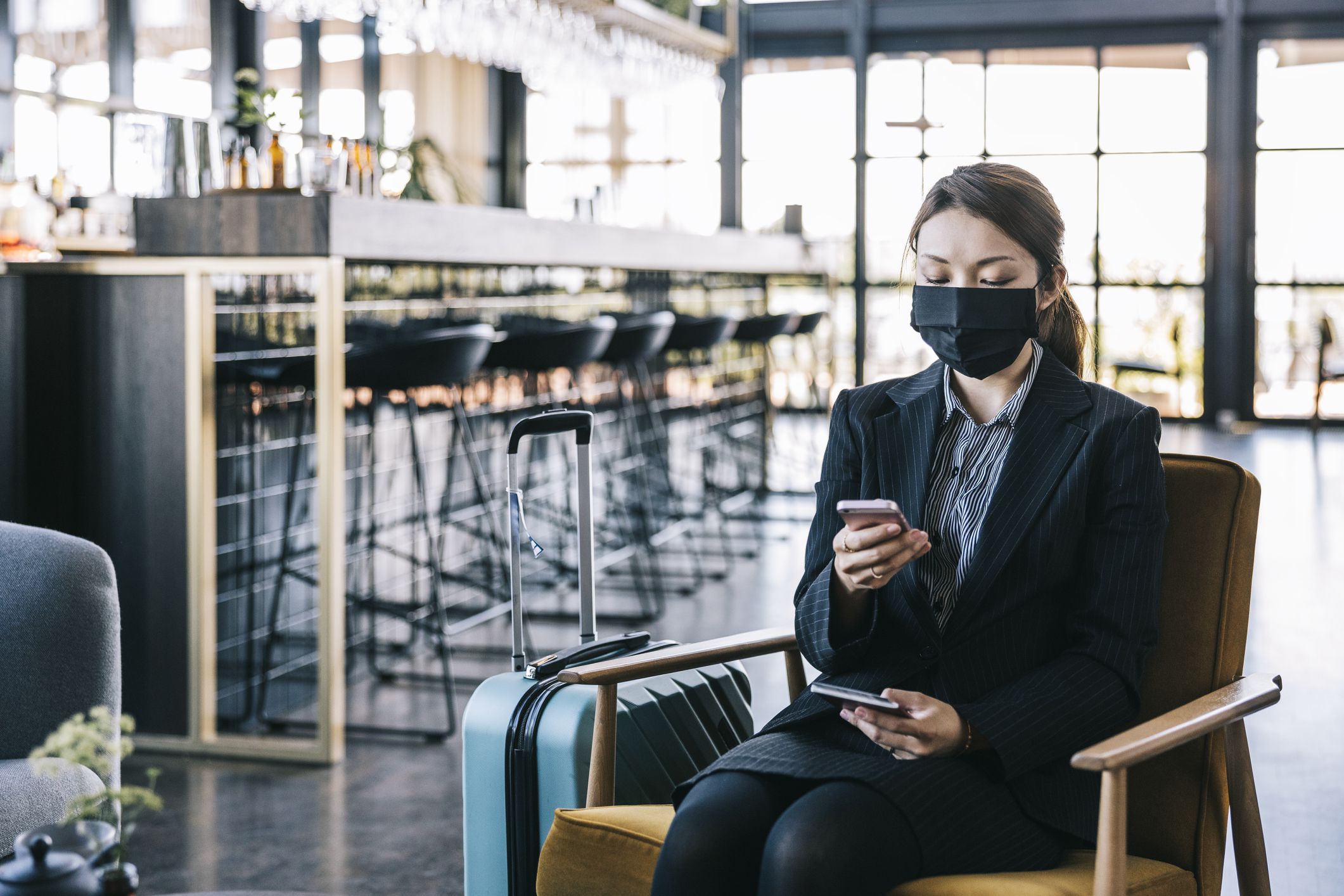 Businesswoman on video call at the airport. Wearing a reusable mask.