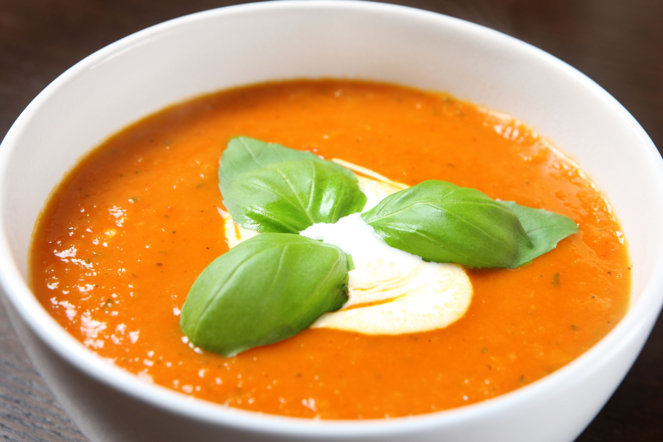A picture of a white bowl full of fresh pepper soup with basil leaves on top
