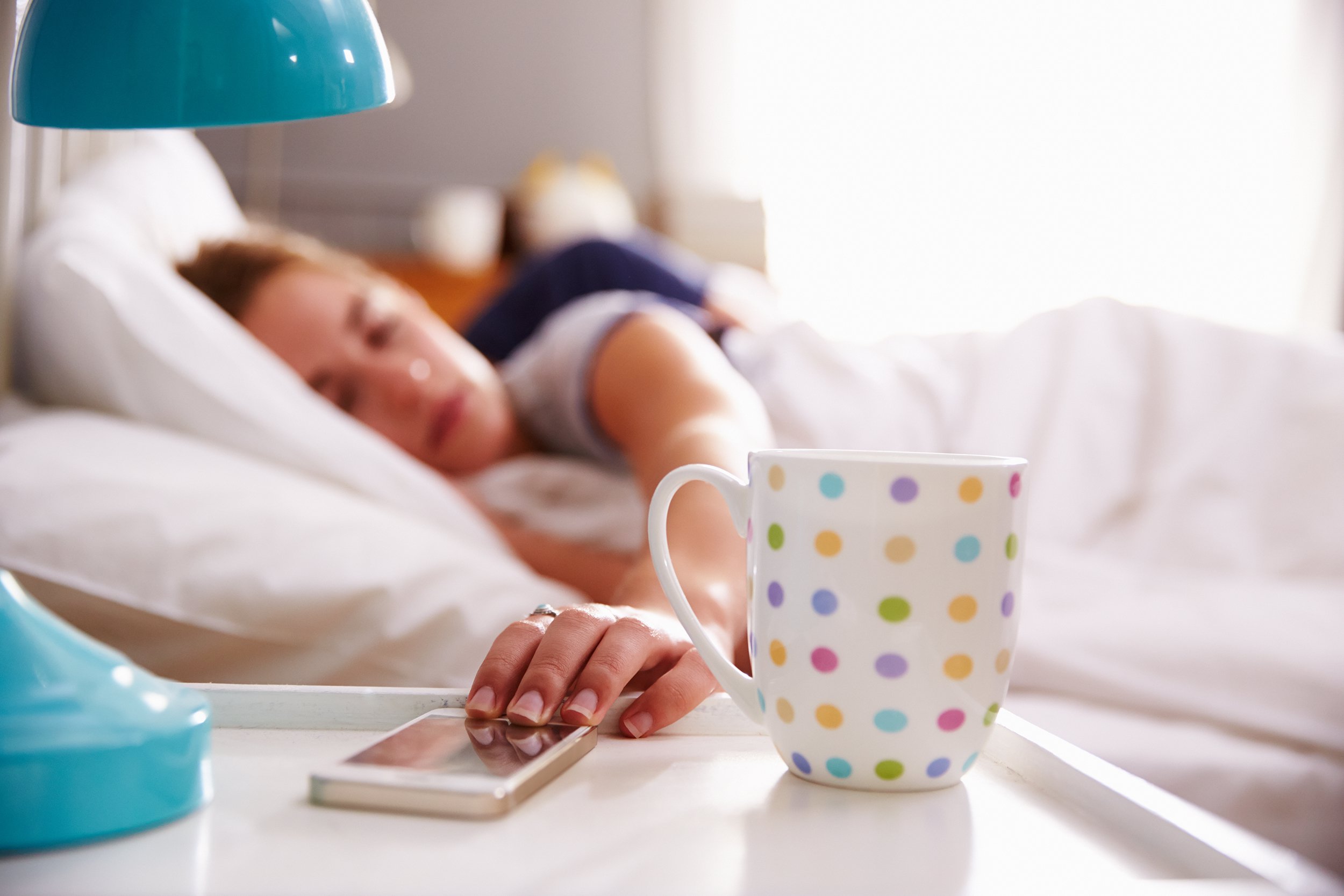 woman in bed reaching for her mobile phone on nightstand