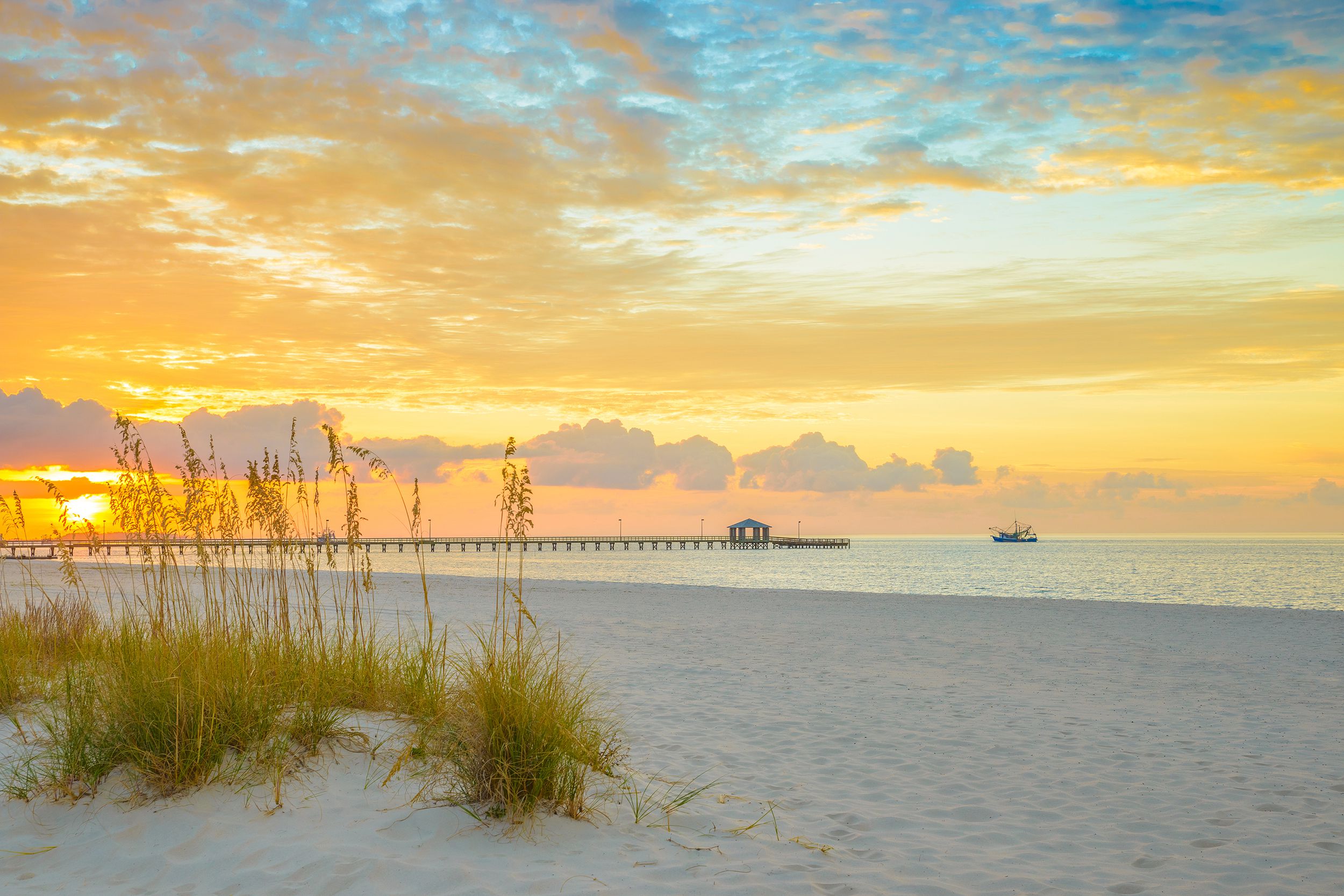 Dramatic golden sunrise on beach of Gulfport, Mississippi with pier and shrimp boat