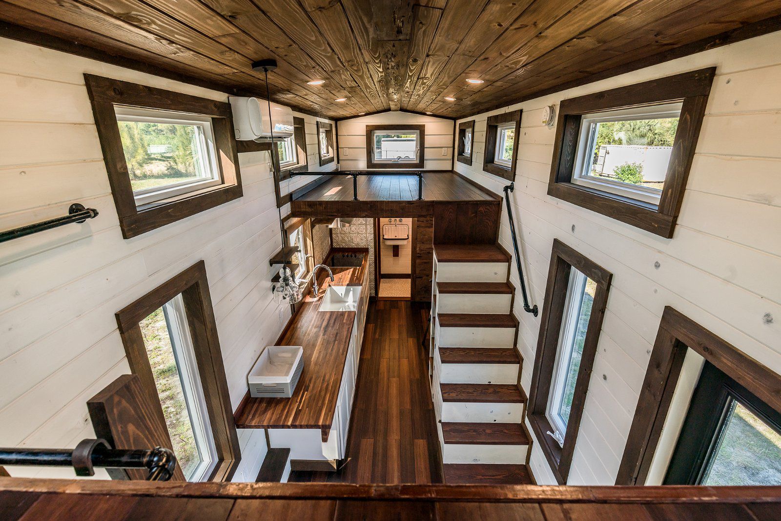 Interior of Farm House Pro, Fellsmere, Florida, large living area with stairs to loft bed, white and dark wooden coloring, sunlight coming through the windows