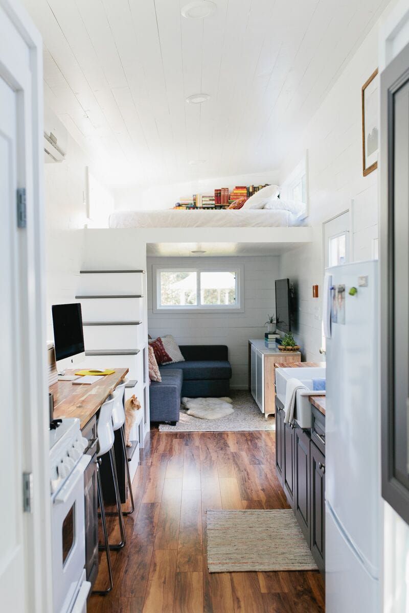 Interior of Golden American Tiny House, Longview, Texas, kitchen with loft bed and nook below in the background, wooden floor with wall coloring and walls
