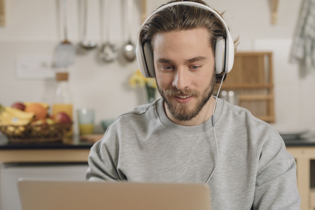 Young man with beard wearing headphones using his laptop.