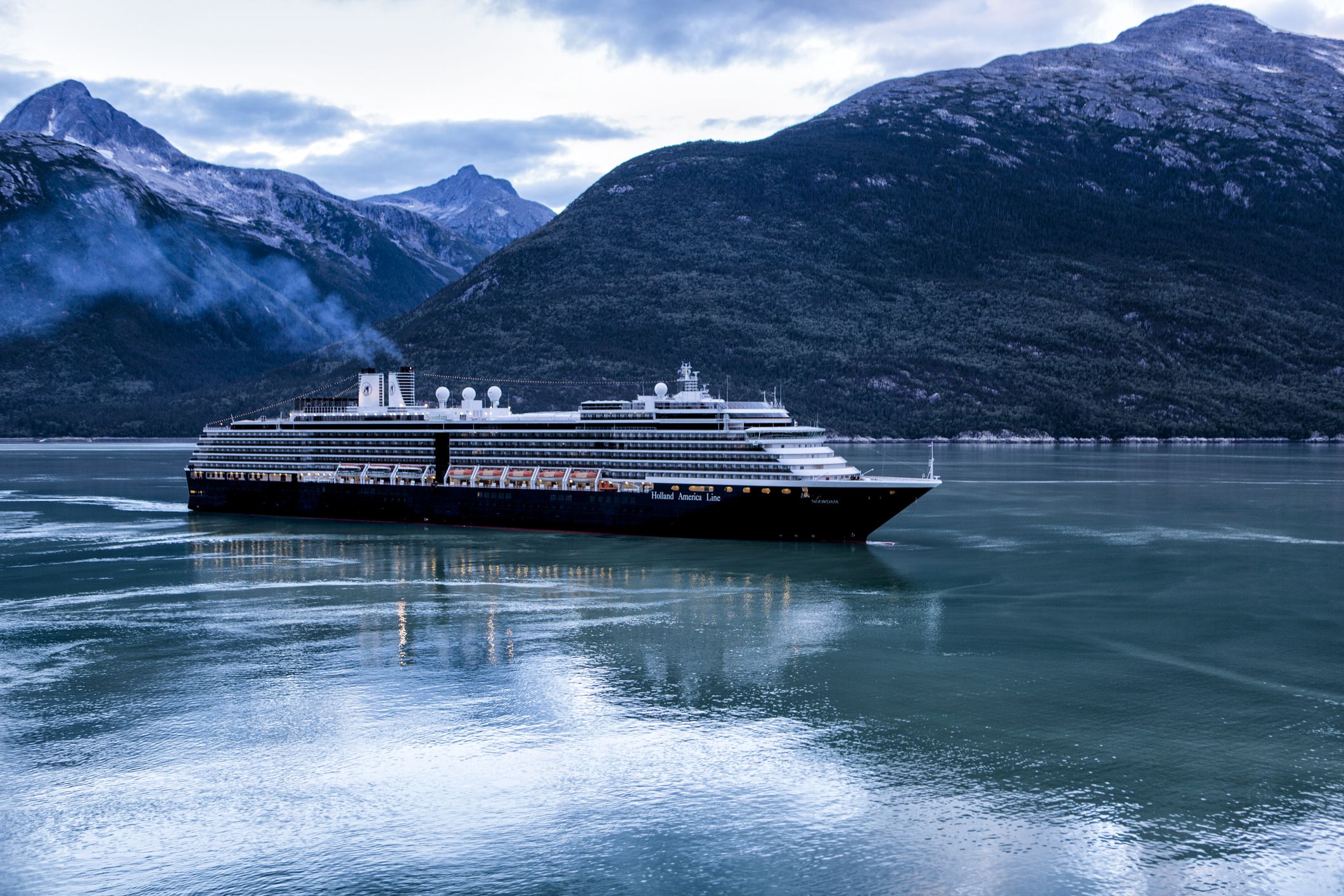 Holland America cruise ship MS Noordam sailing into Skagway, Alaska at dawn with mountains in the background on a cloudy day