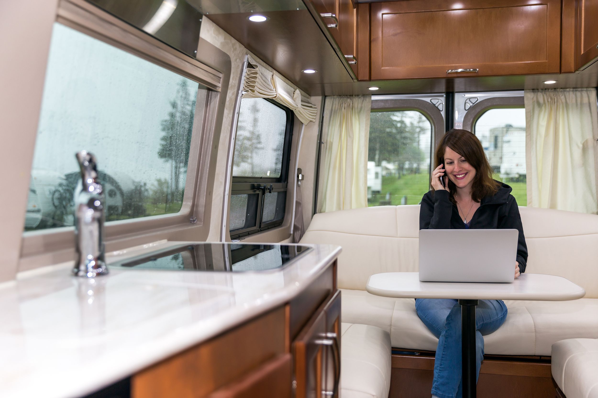 young woman talking on phone and using laptop inside super fancy motorhome