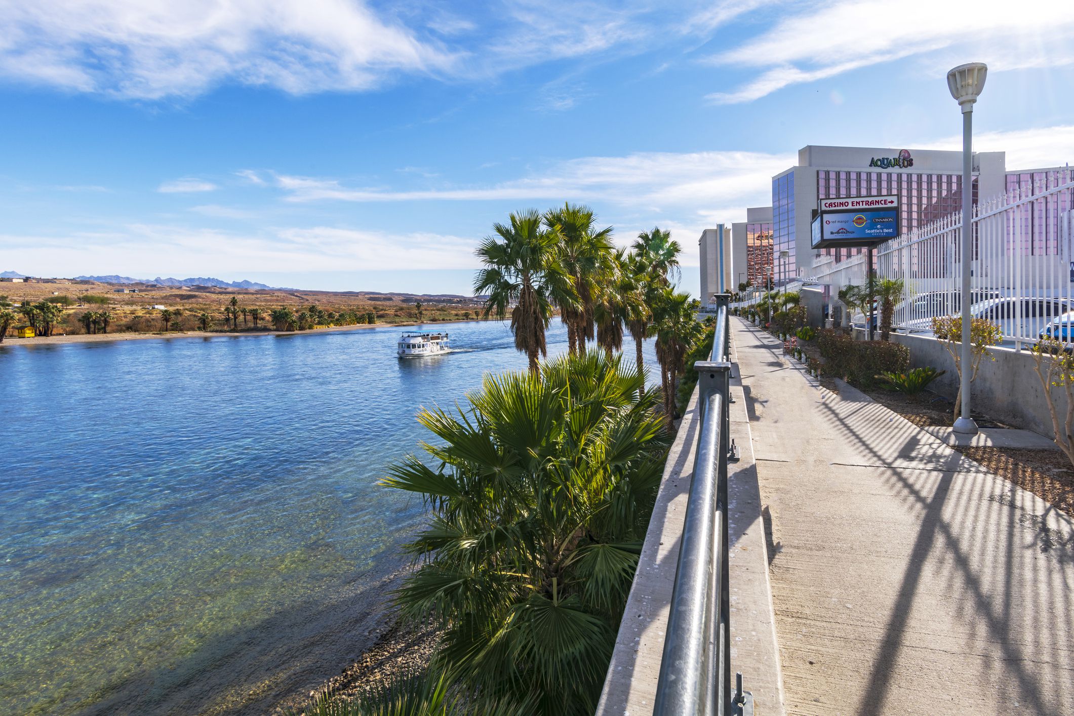 Resort casinos on walkway along Colorado River in Laughlin, Nevada with boat on river and scenic mountains in background