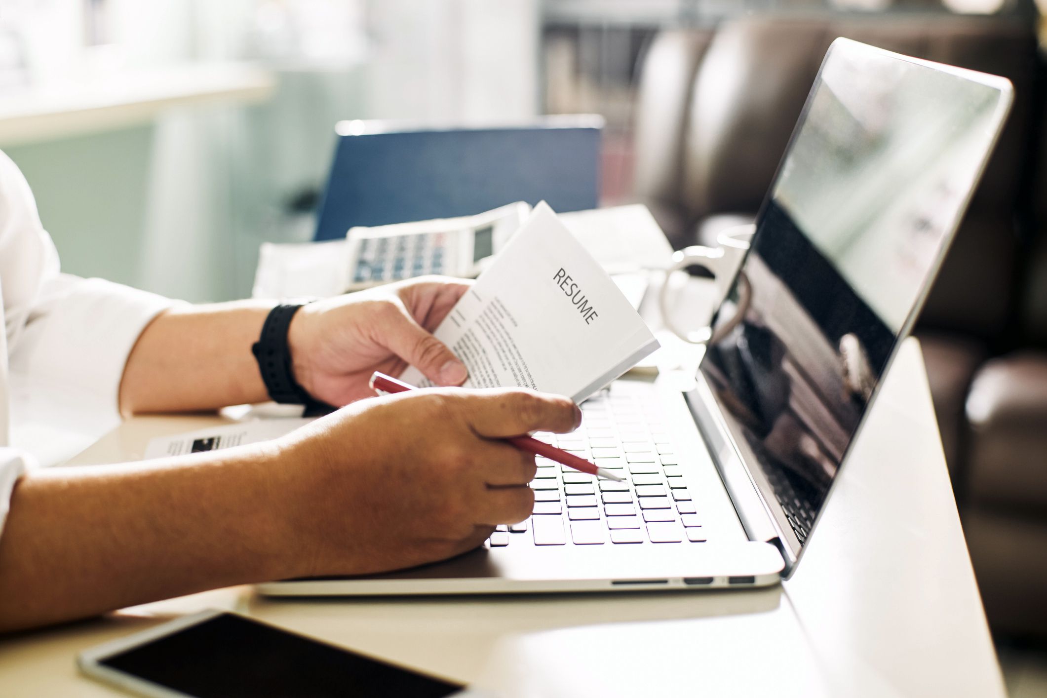Hands holding resume with pencil in hand in front of open laptop