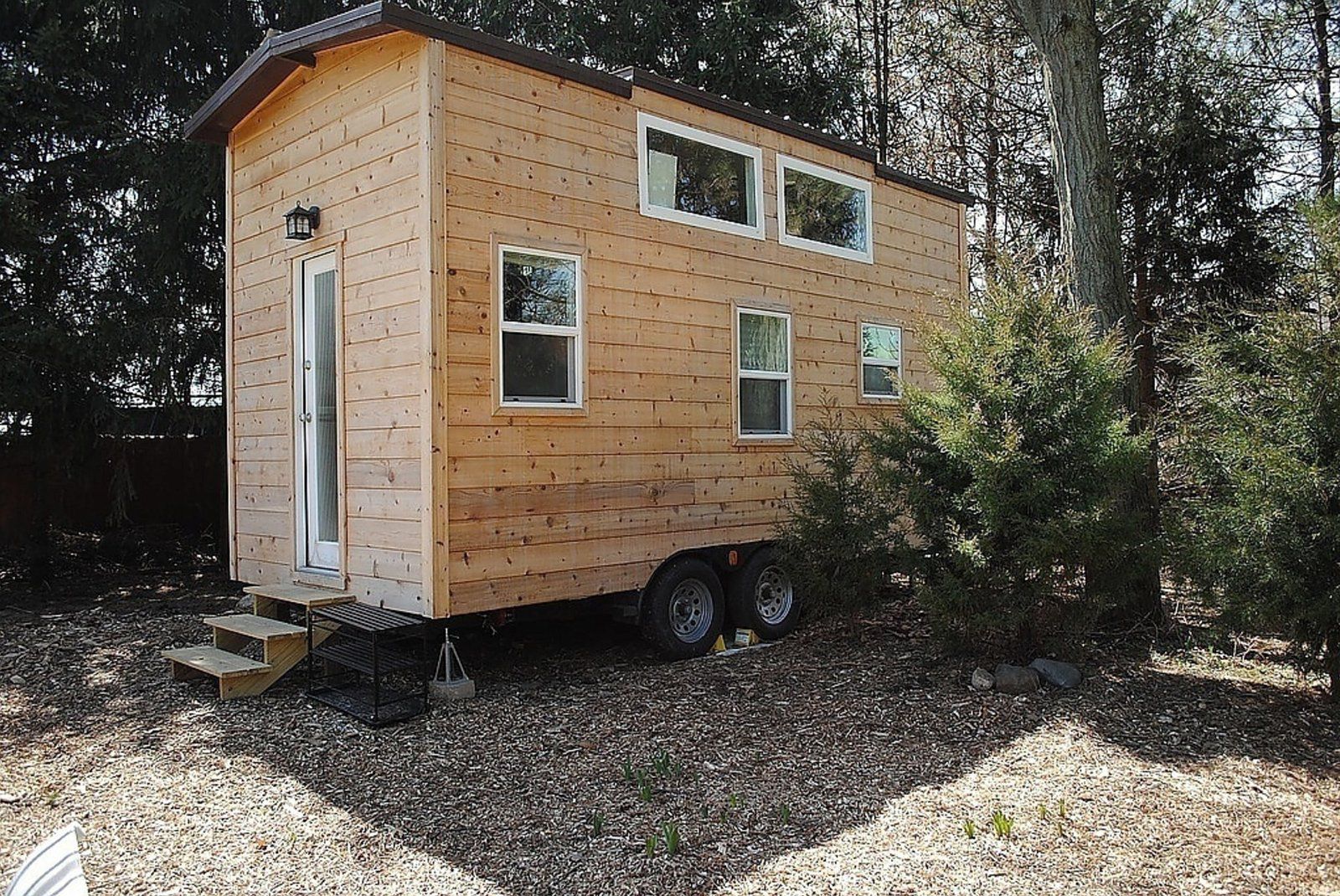Front and side exterior of Roomy 18' THOW, Chicago, surrounded by trees, on mulch and grass, on a sunny day during summer