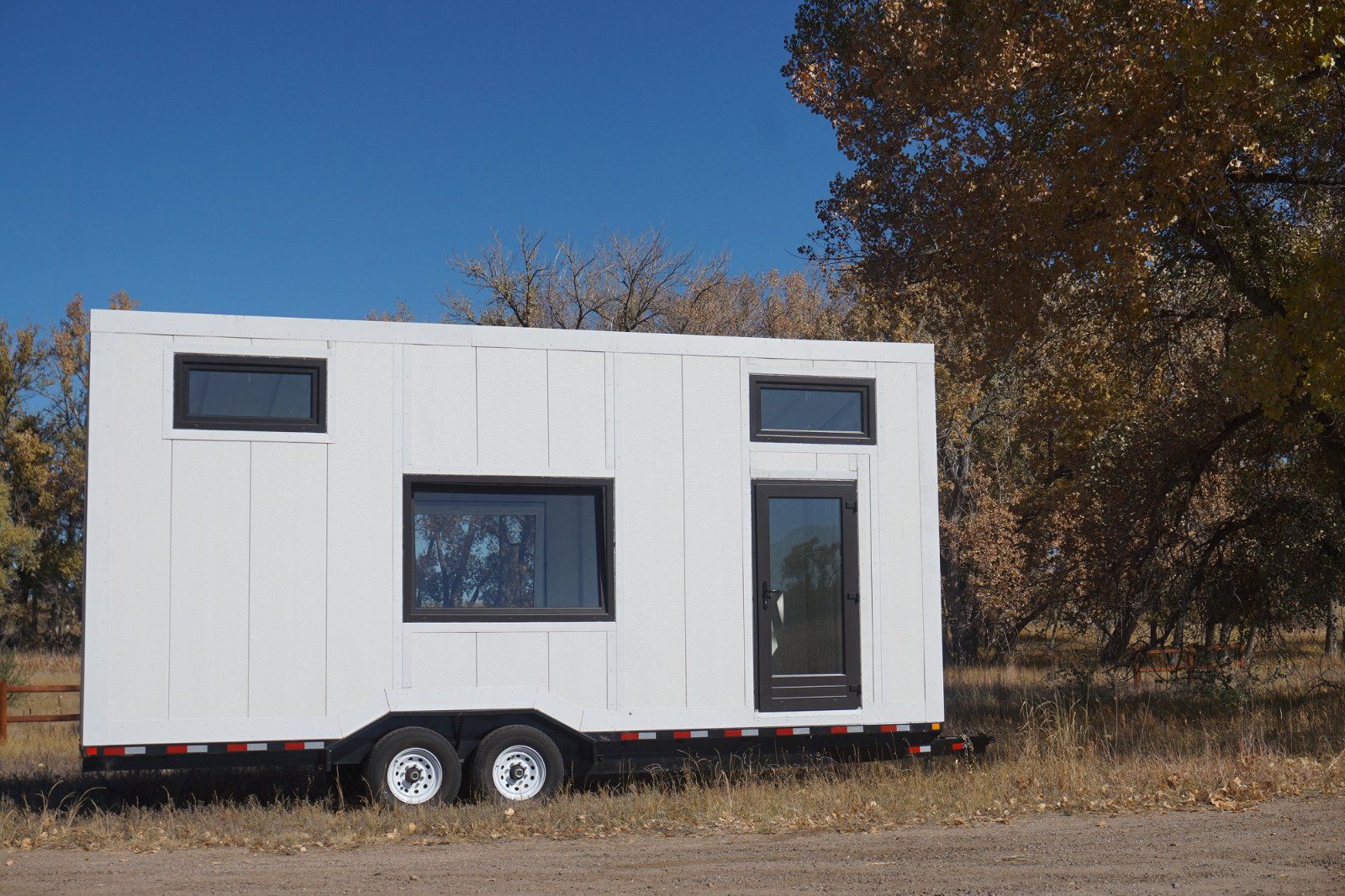 Side exterior of SmartShell Tiny Home Shell, Nashville, white panels with windows, on grass surrounded by trees during autumn