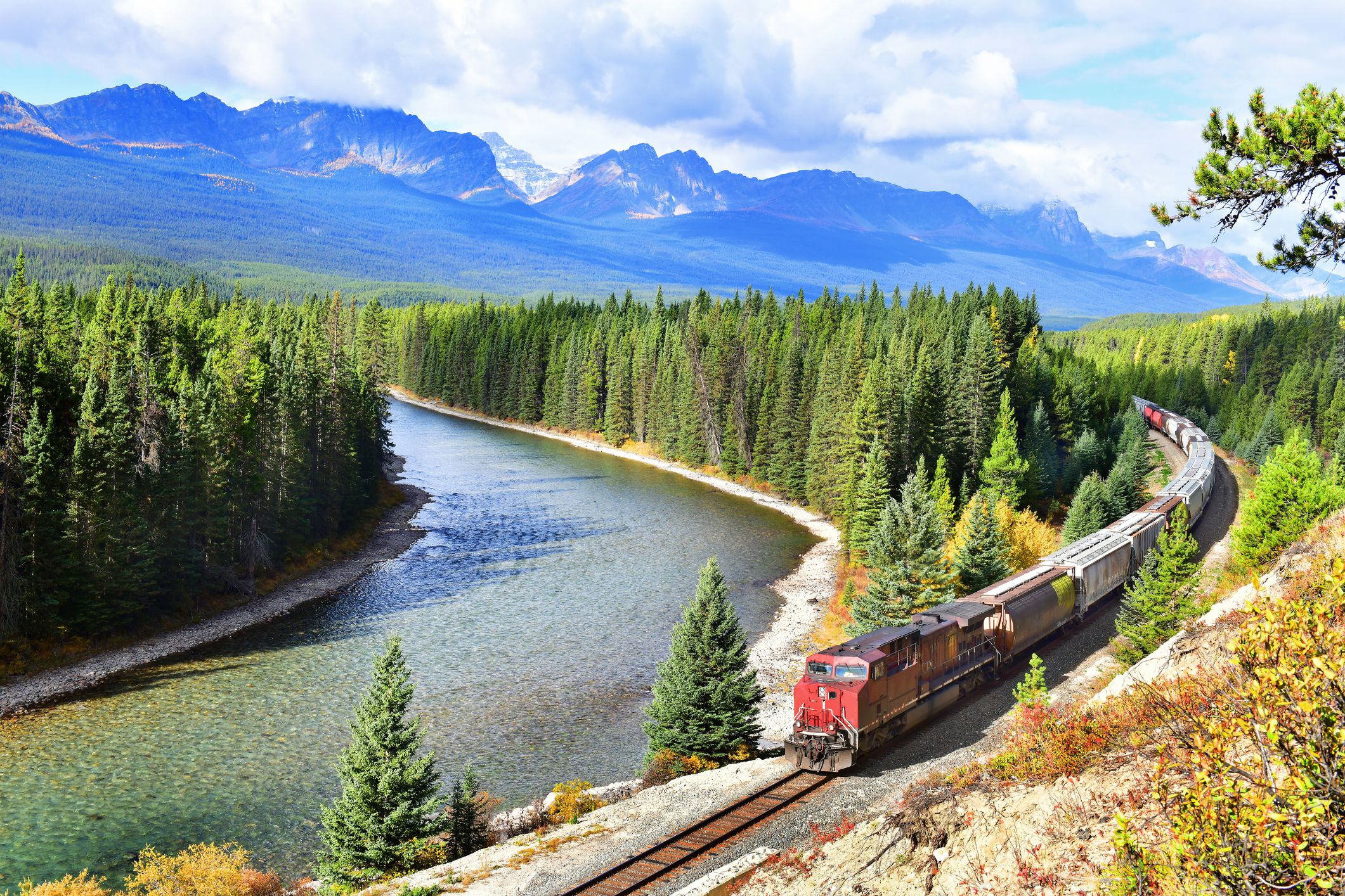Train on the Canadian Pacific Railway moving along Bow River in the Canadian Rockies, Banff National Park on a sunny summer day with the mountains in the background