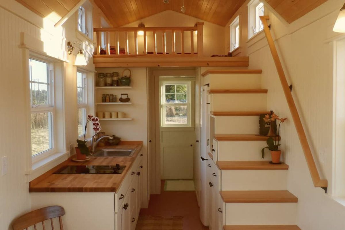 Interior of Unita, Eugene, Oregon, kitchenette on the left with stairs to loft on the right, loft bed in the background, white and light wooden coloring and well-lit