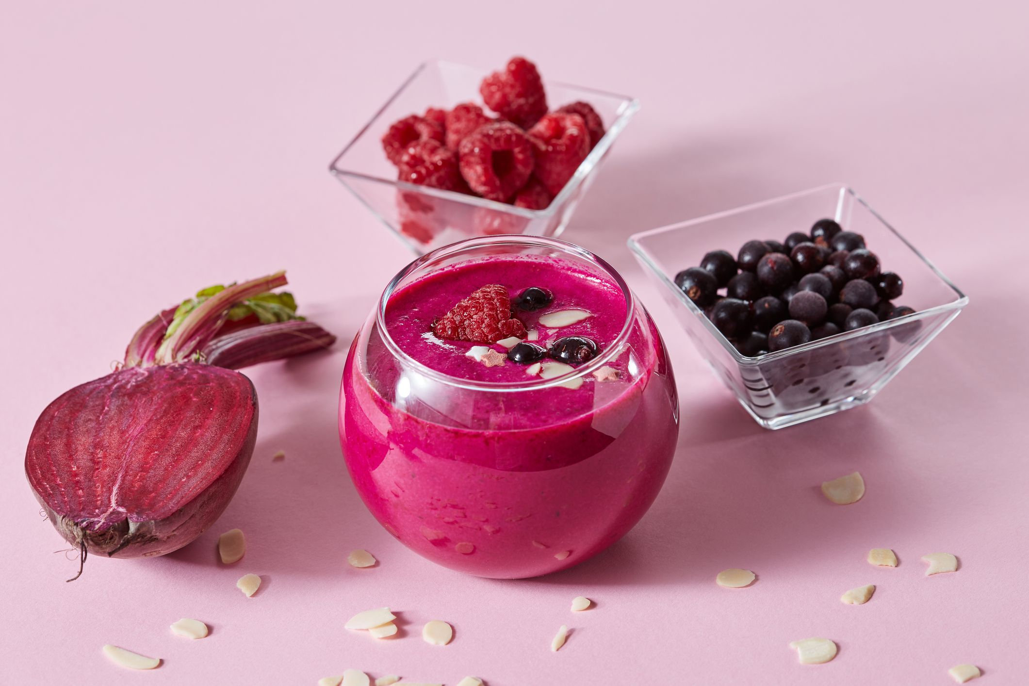 Vegetarian healthy smoothies from red berries and beetroot with almond plates in a glass cup on a pink paper background.