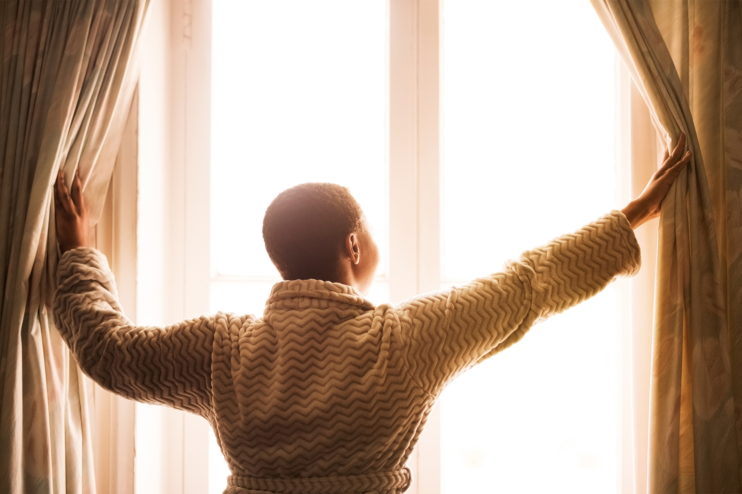 woman opening curtains in the morning waking up