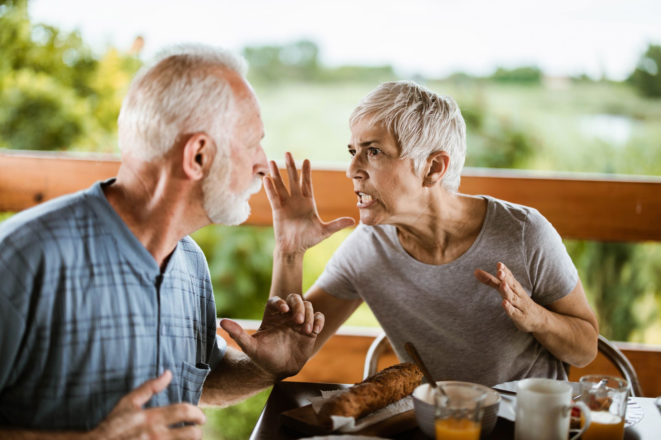 Frustrated senior couple arguing while having problems during breakfast on a balcony.