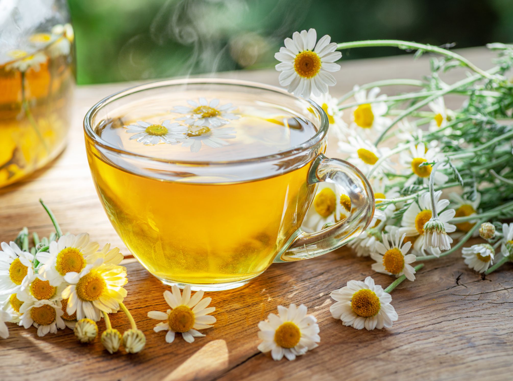 Herbal chamomile tea and chamomile flowers near teapot and tea glass. Rural or countryside background.