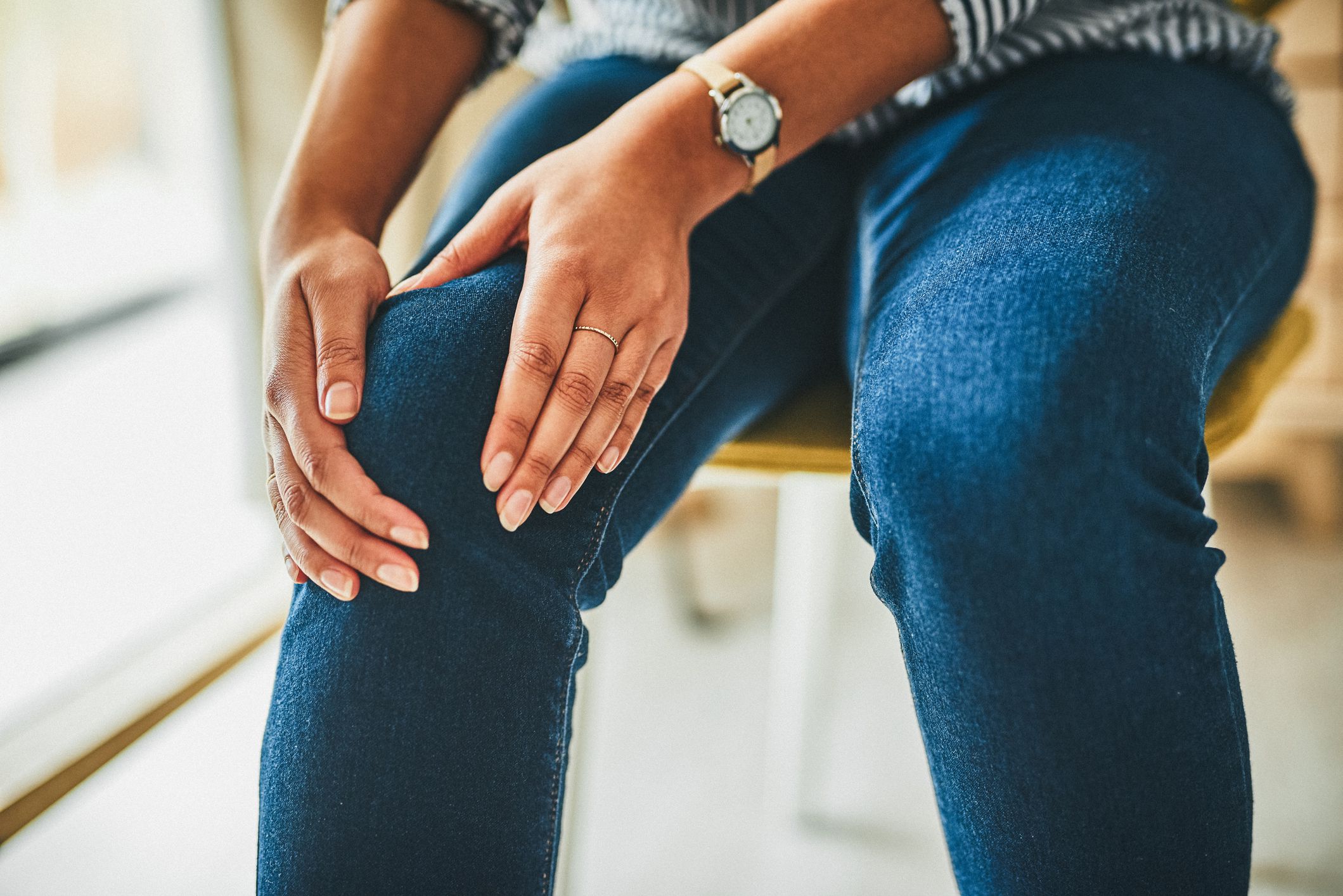 Closeup shot of an unrecognisable woman rubbing her knee in pain while working from home