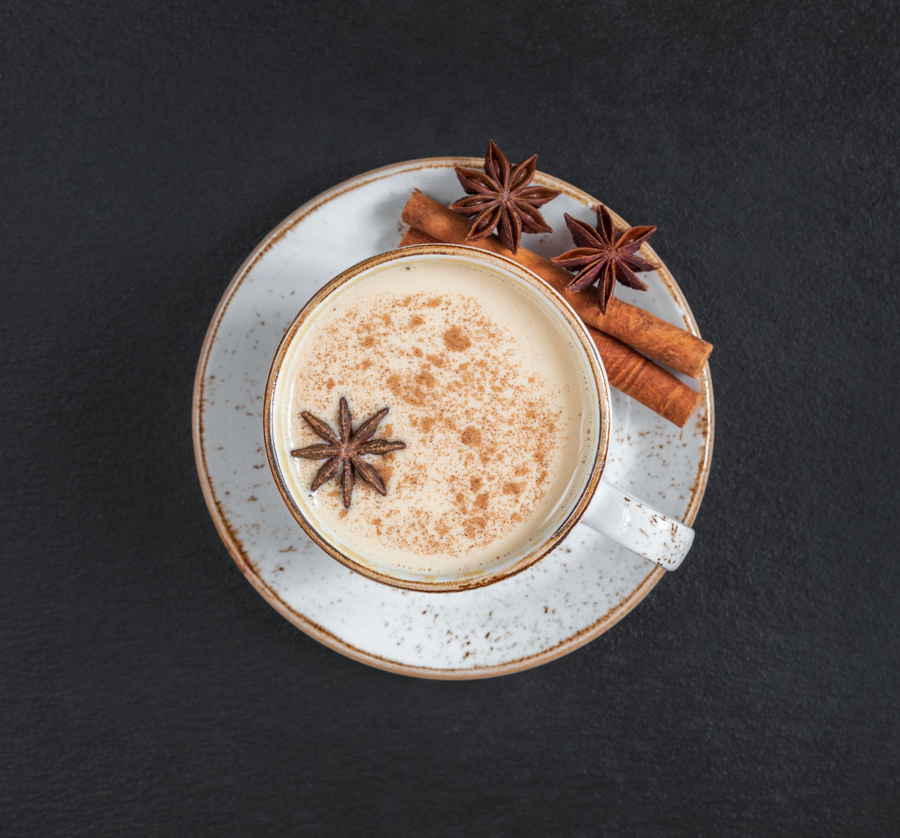 Masala chai tea on a dark background close up. Traditional Indian hot drink with milk and spices. Top view, flat lay.