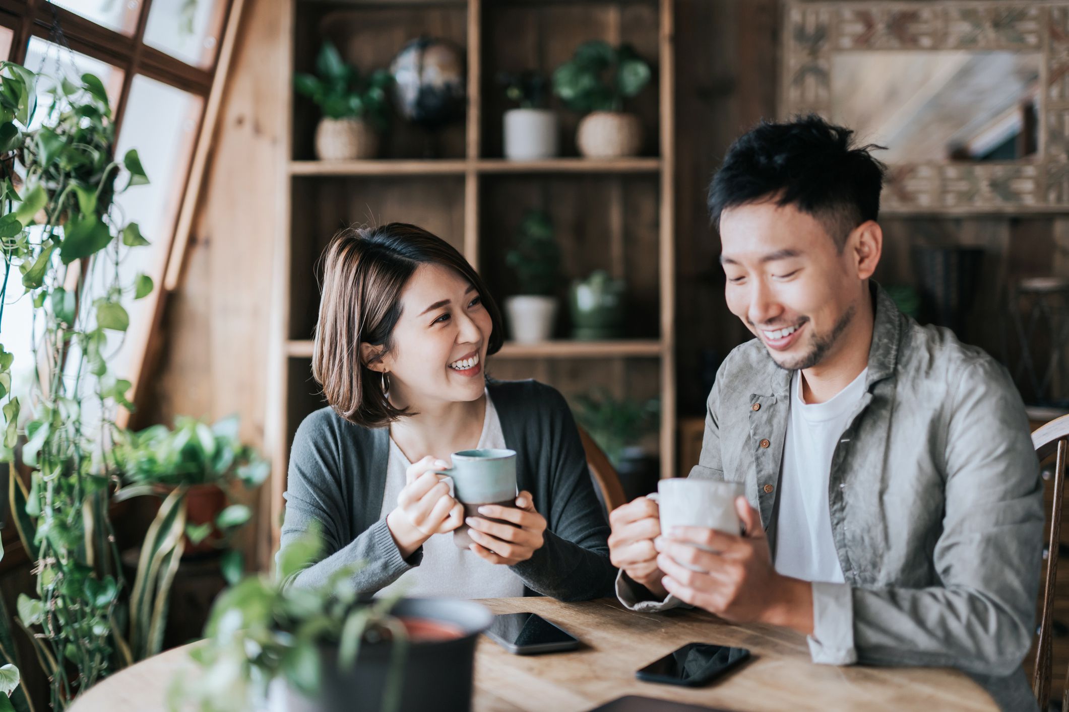 Happy young Asian couple having a coffee date in cafe, drinking coffee and chatting. Enjoying a relaxing moment together